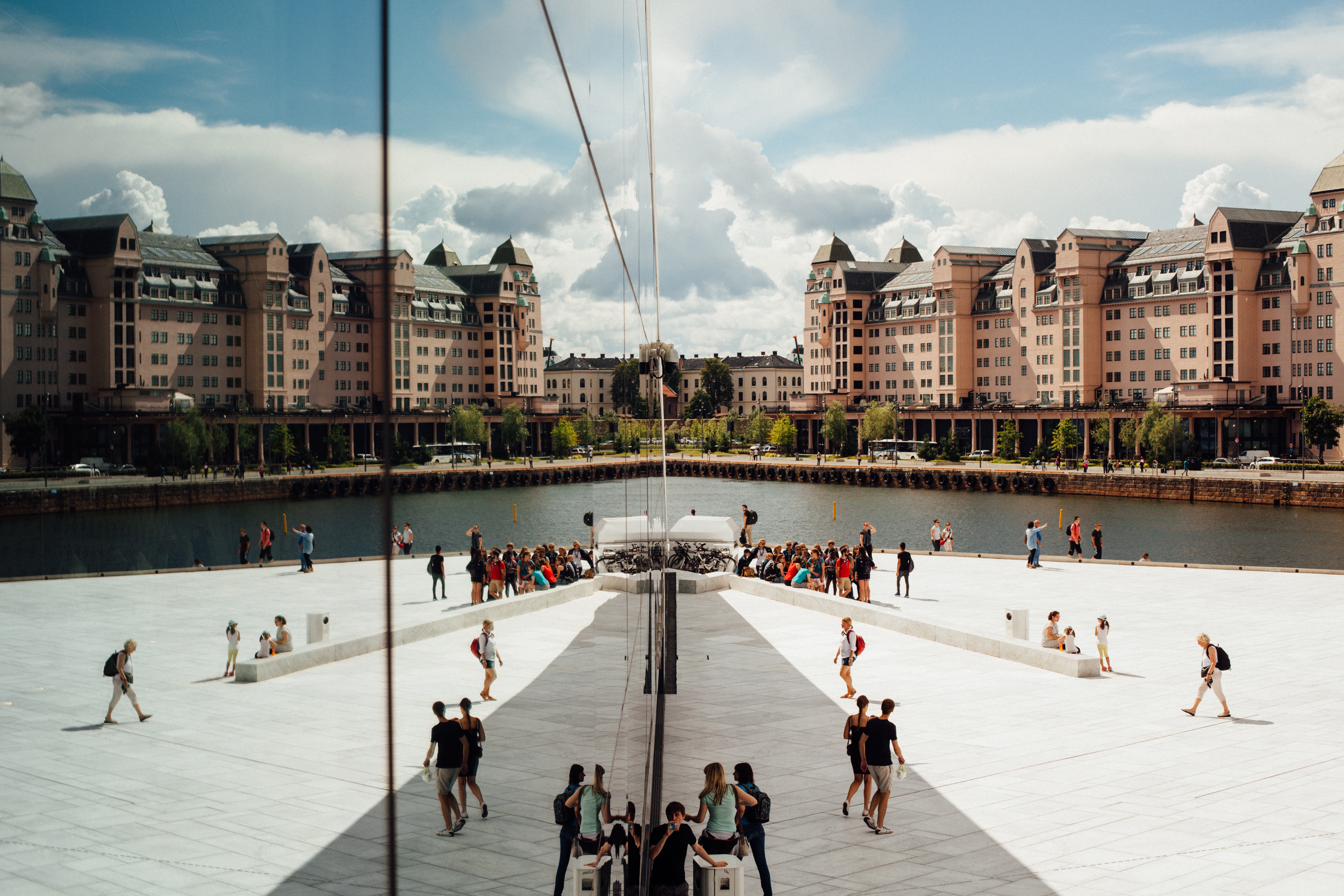People walking on a waterfront with buildings reflected in glass HD Wallpaper