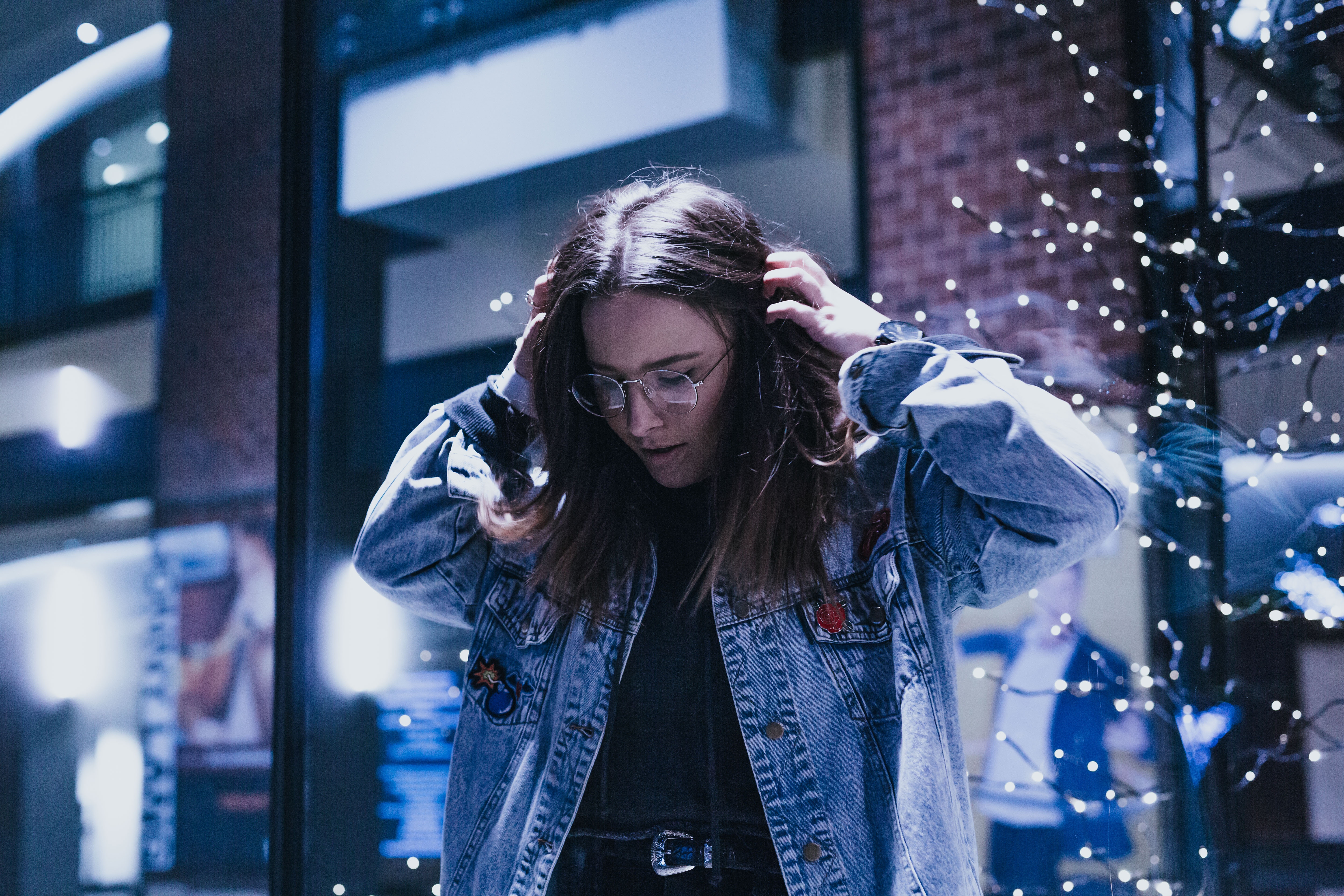 Woman in denim jacket with glasses and Christmas lights HD Wallpaper