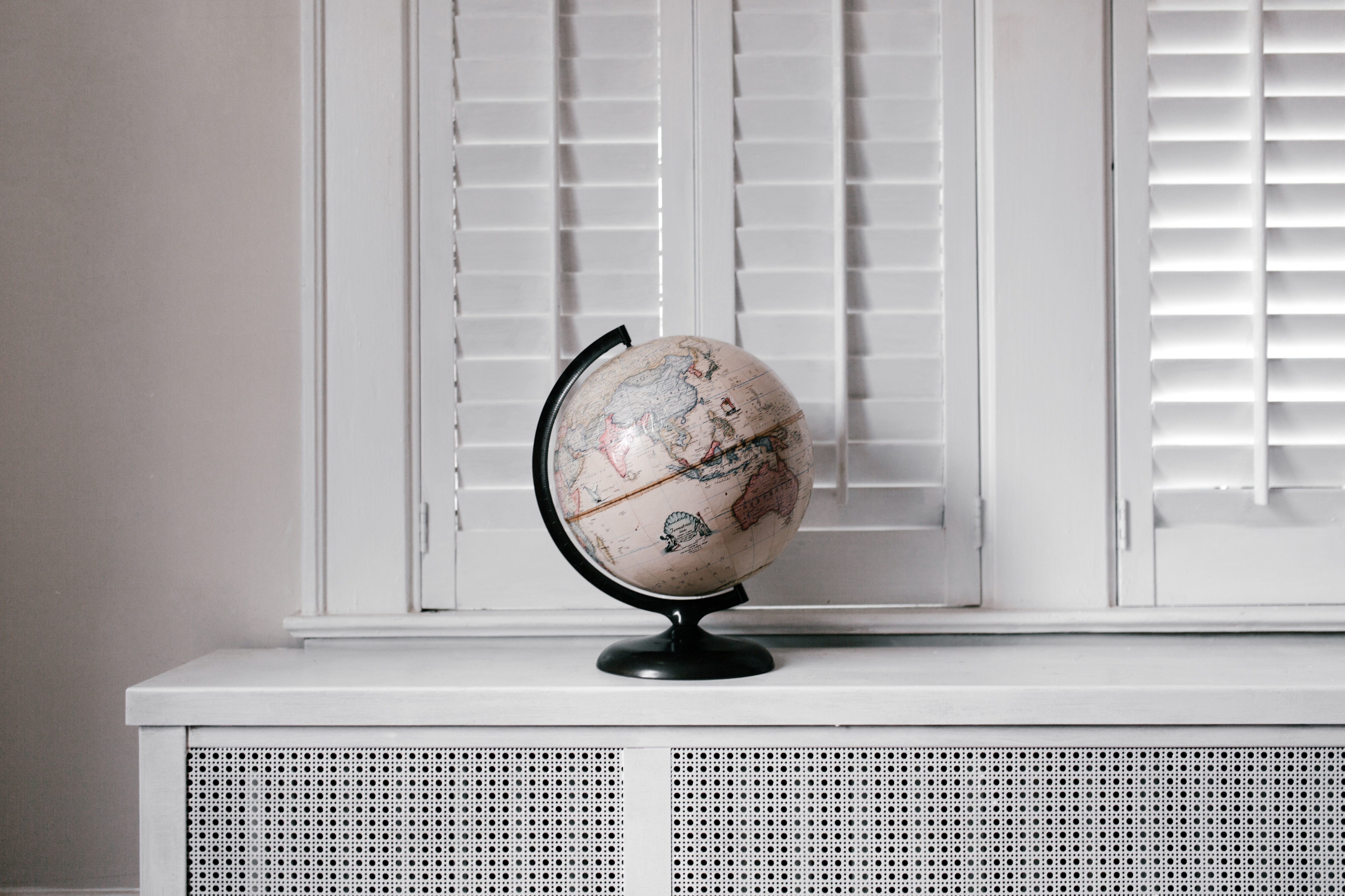 Globe on a white radiator cover in front of shutters HD Wallpaper