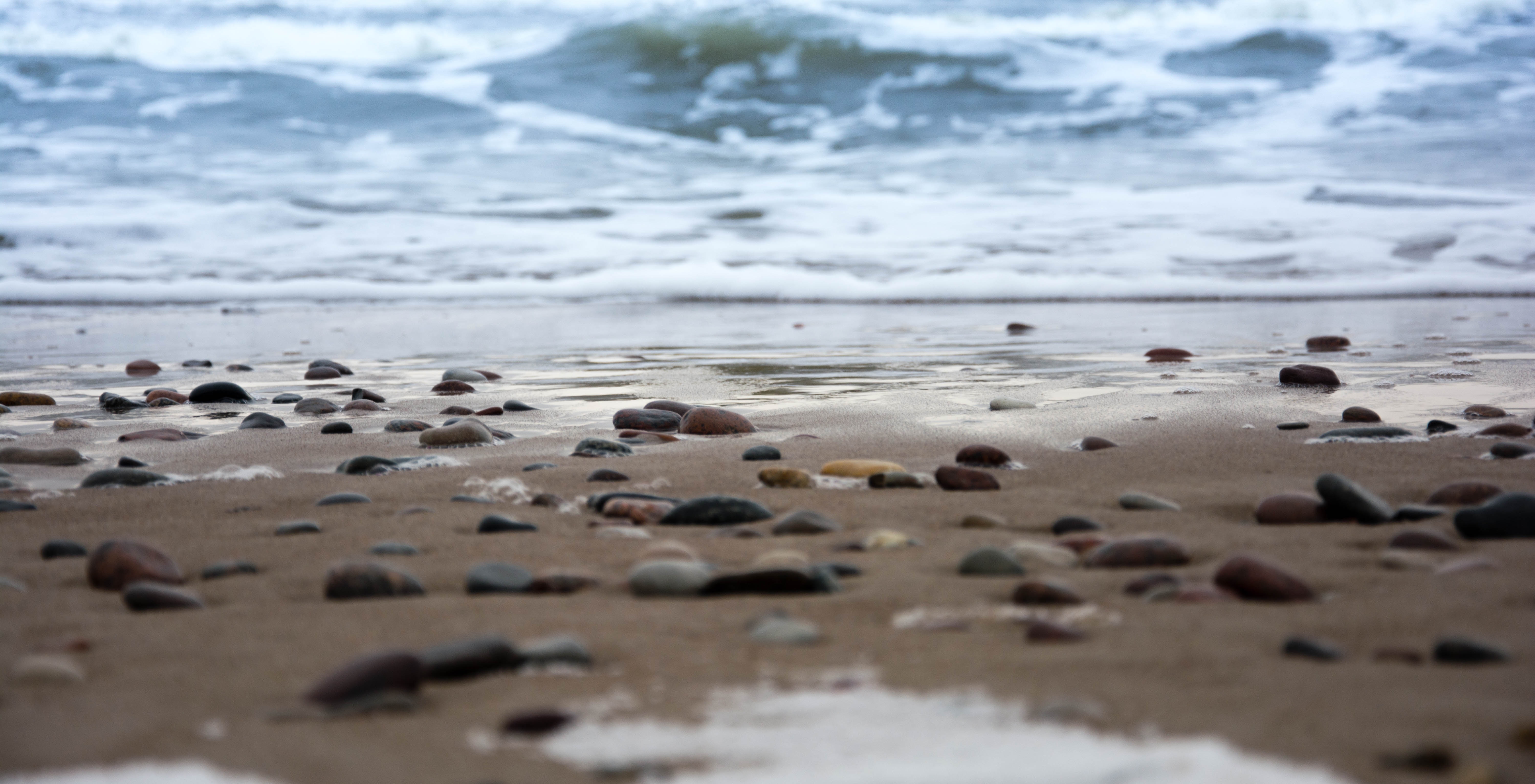 Pebble beach with ocean waves and foam HD Wallpaper