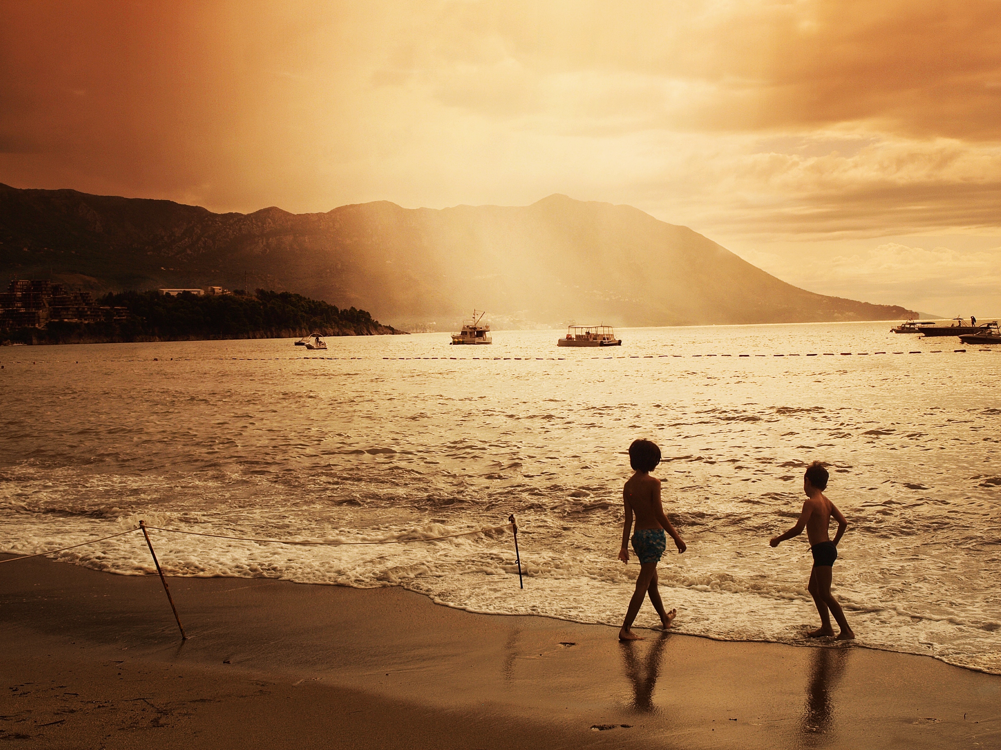 Two children walk on a beach at sunset HD Wallpaper