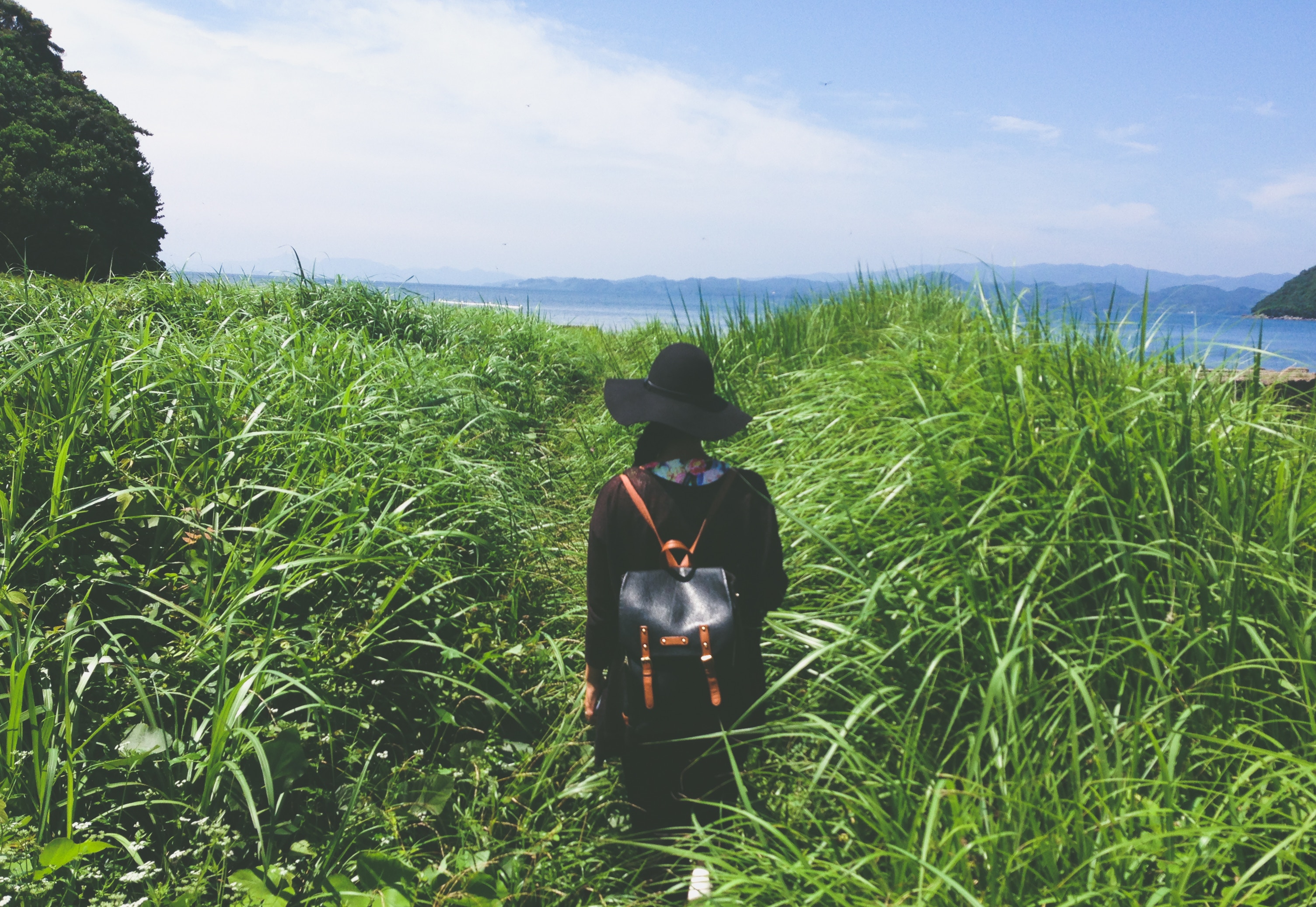 Woman with backpack and hat walking on grassy path HD Wallpaper