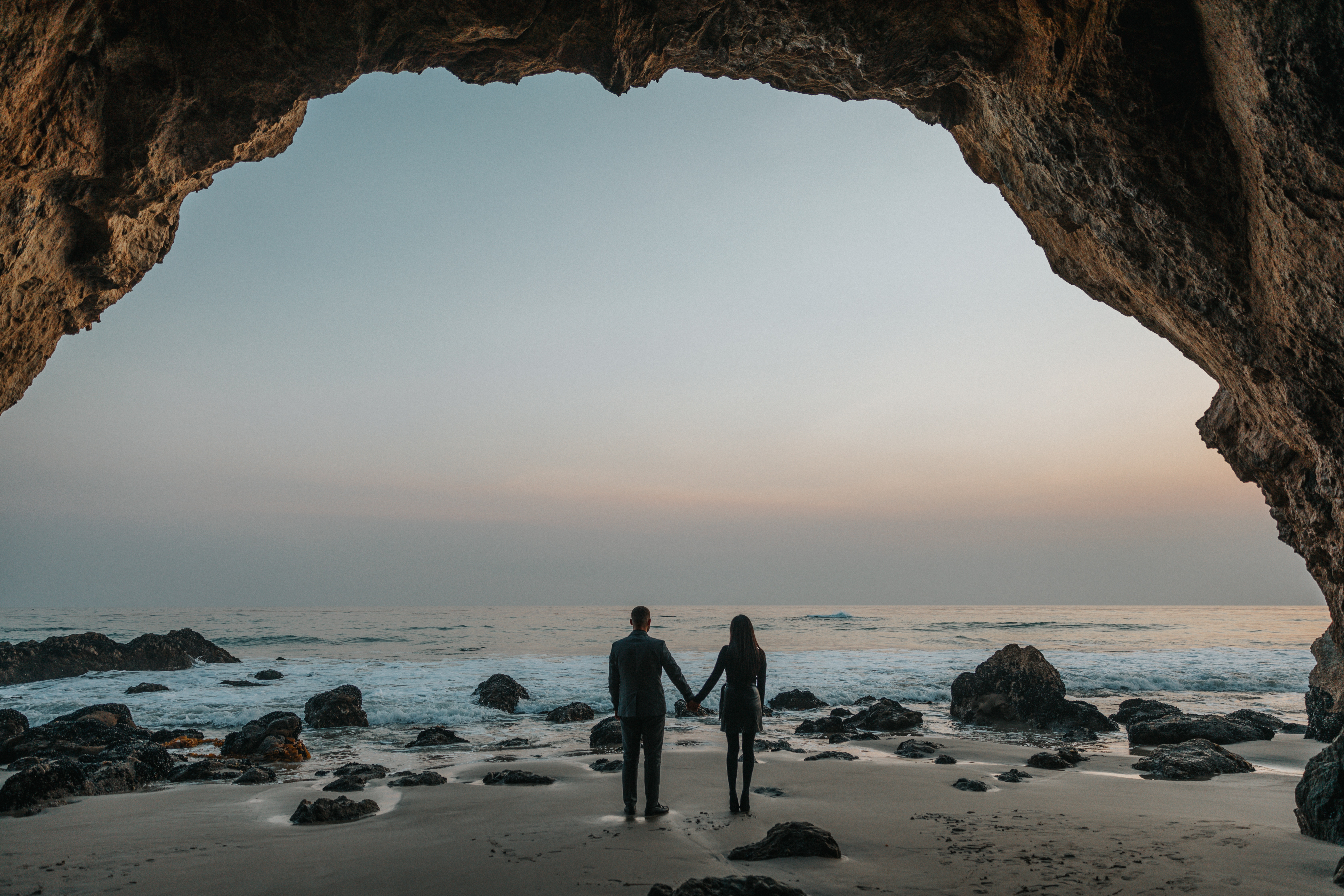 Couple holding hands in a cave at sunset HD Wallpaper