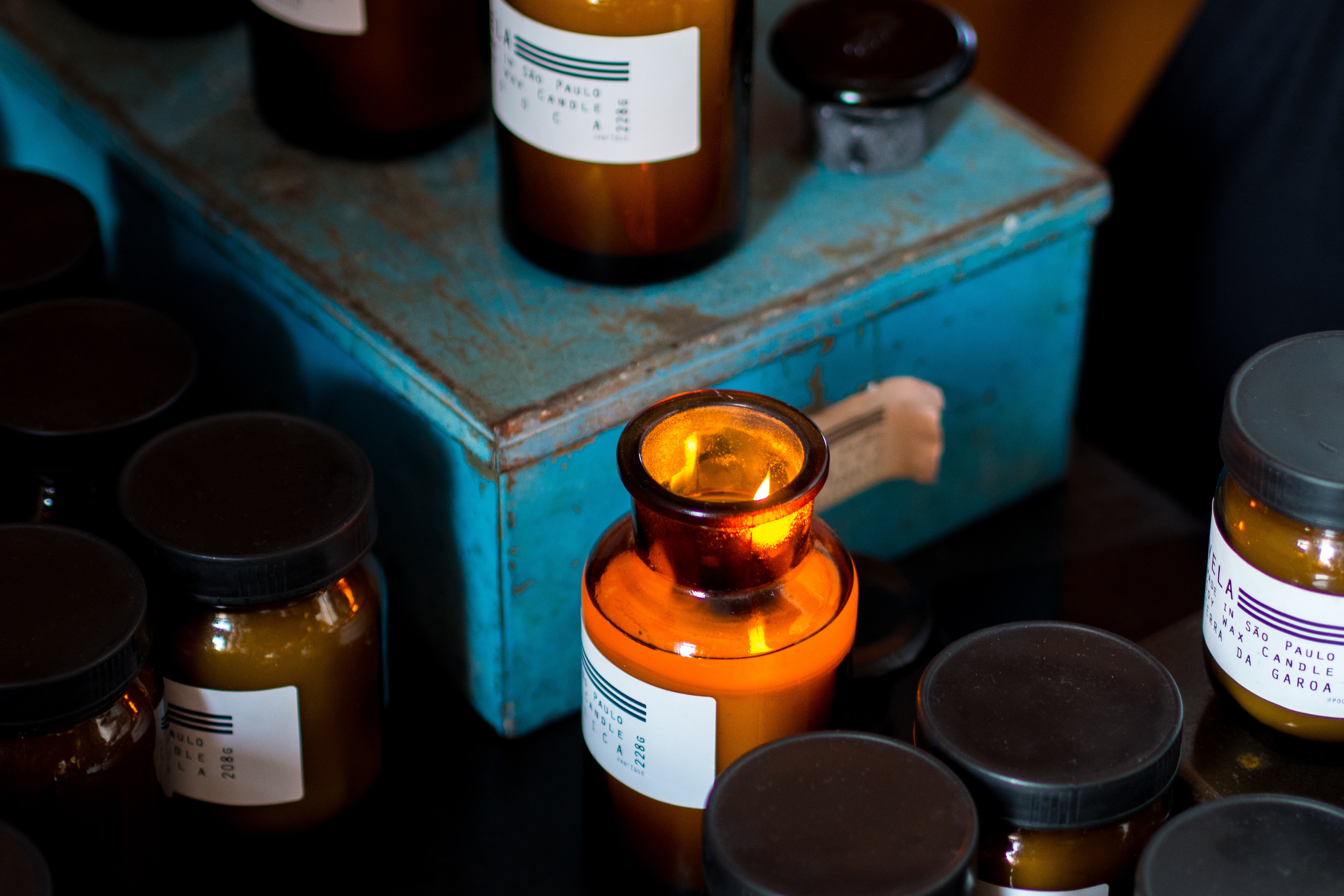 Burning candle in amber glass jar on blue metal box HD Wallpaper