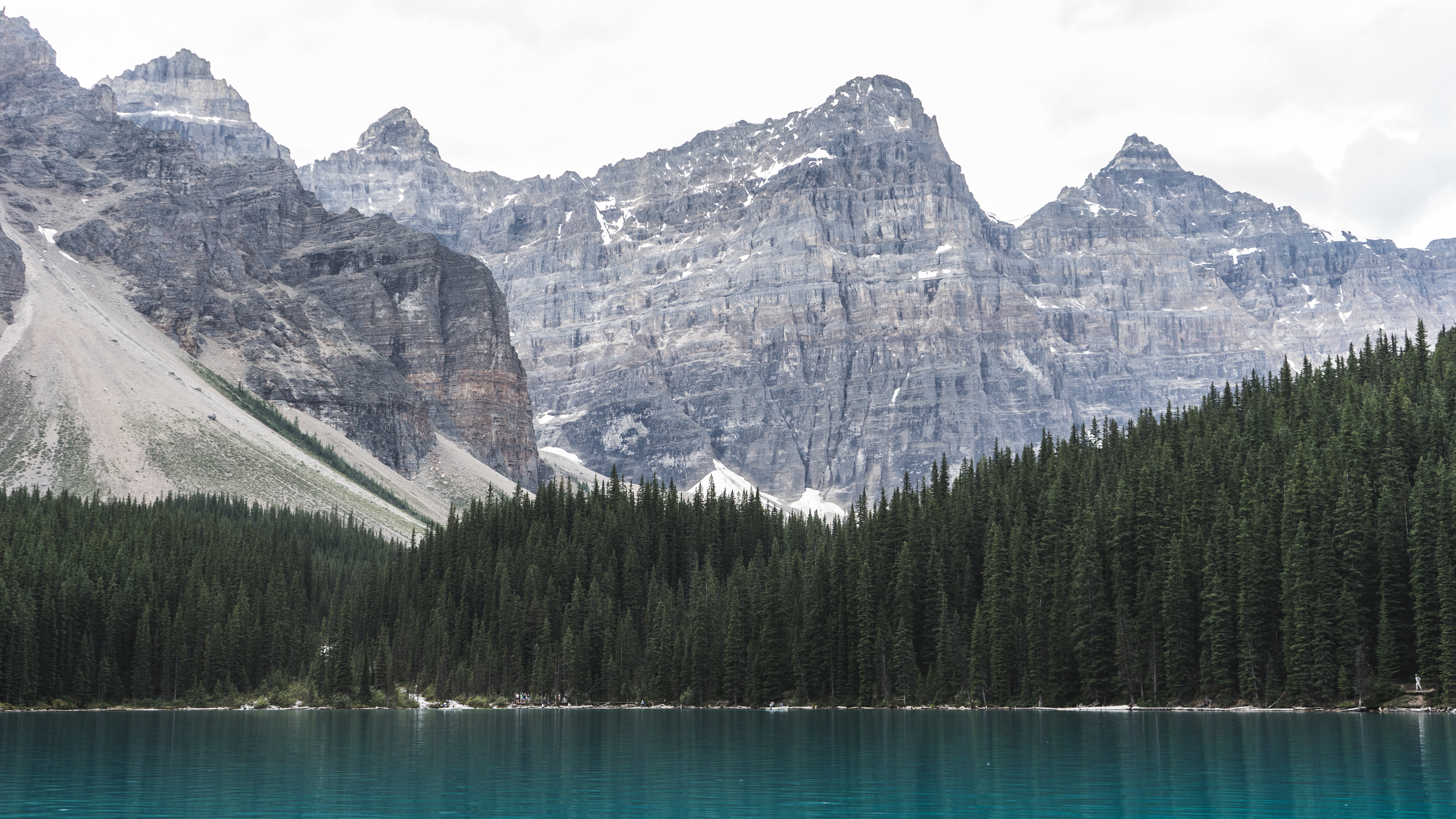 Turquoise lake and pine forest at the base of rugged mountains HD Wallpaper