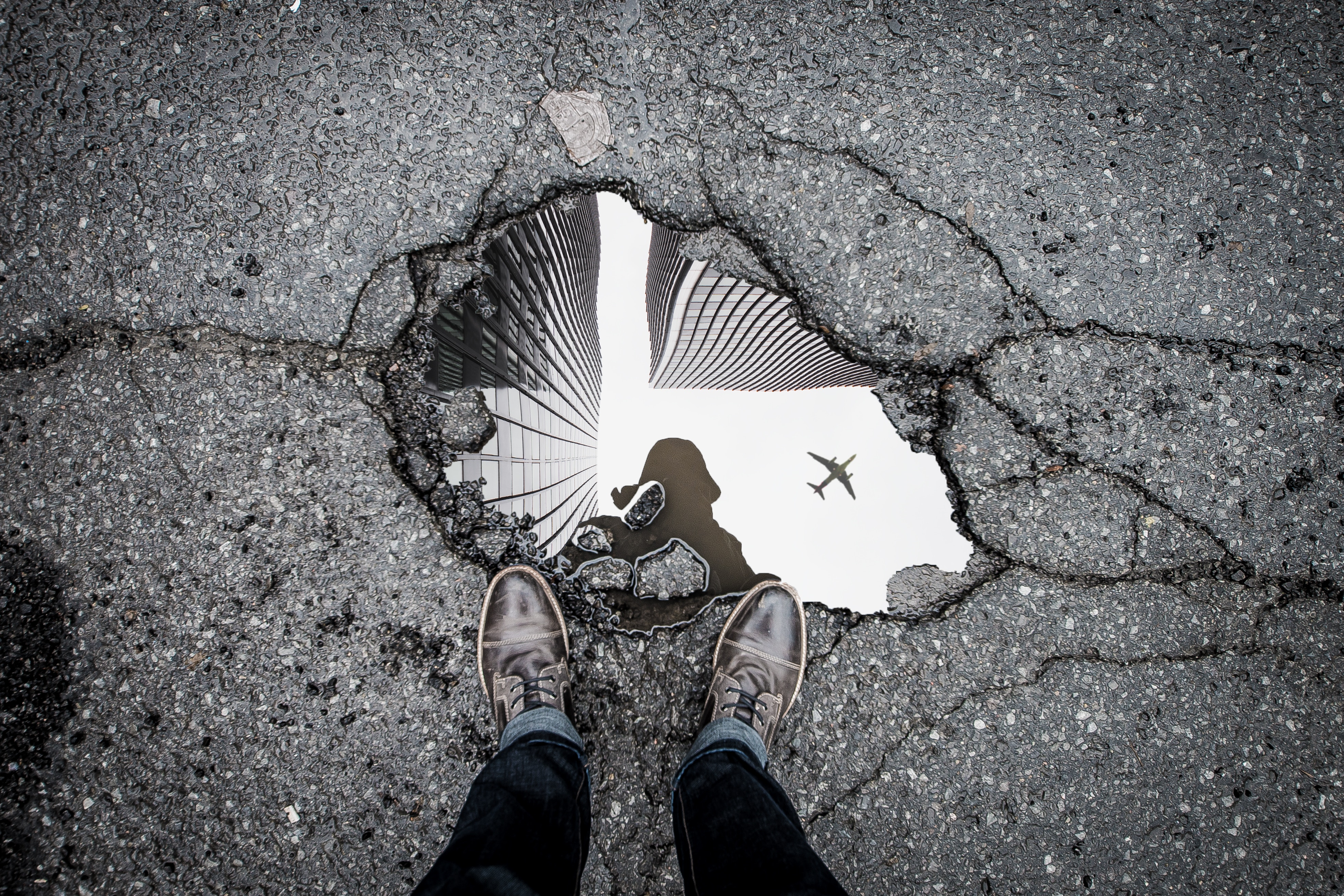 Man's reflection in a pothole with skyscrapers and airplane HD Wallpaper