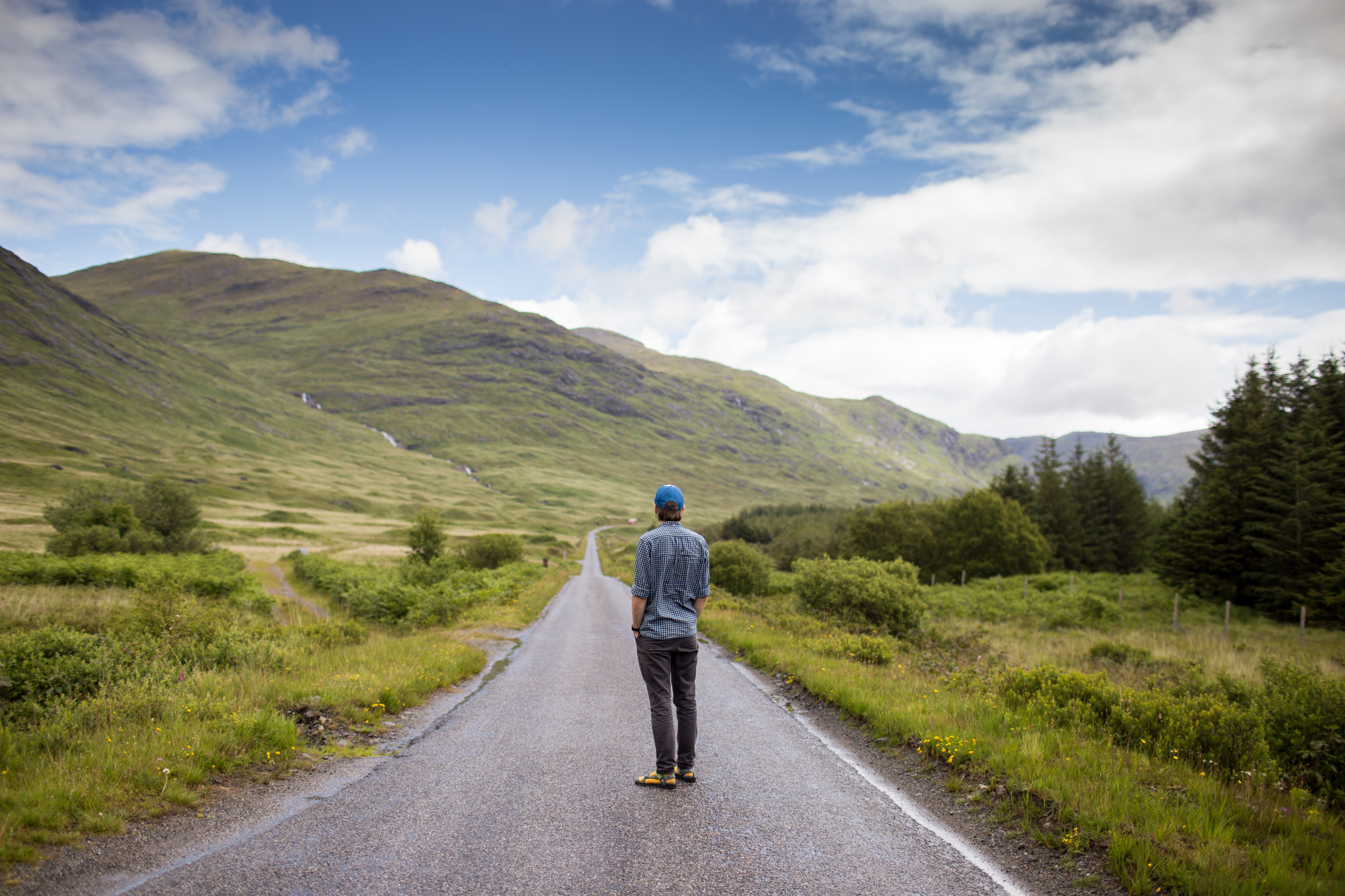 Man standing on a road in a mountainous landscape HD Wallpaper