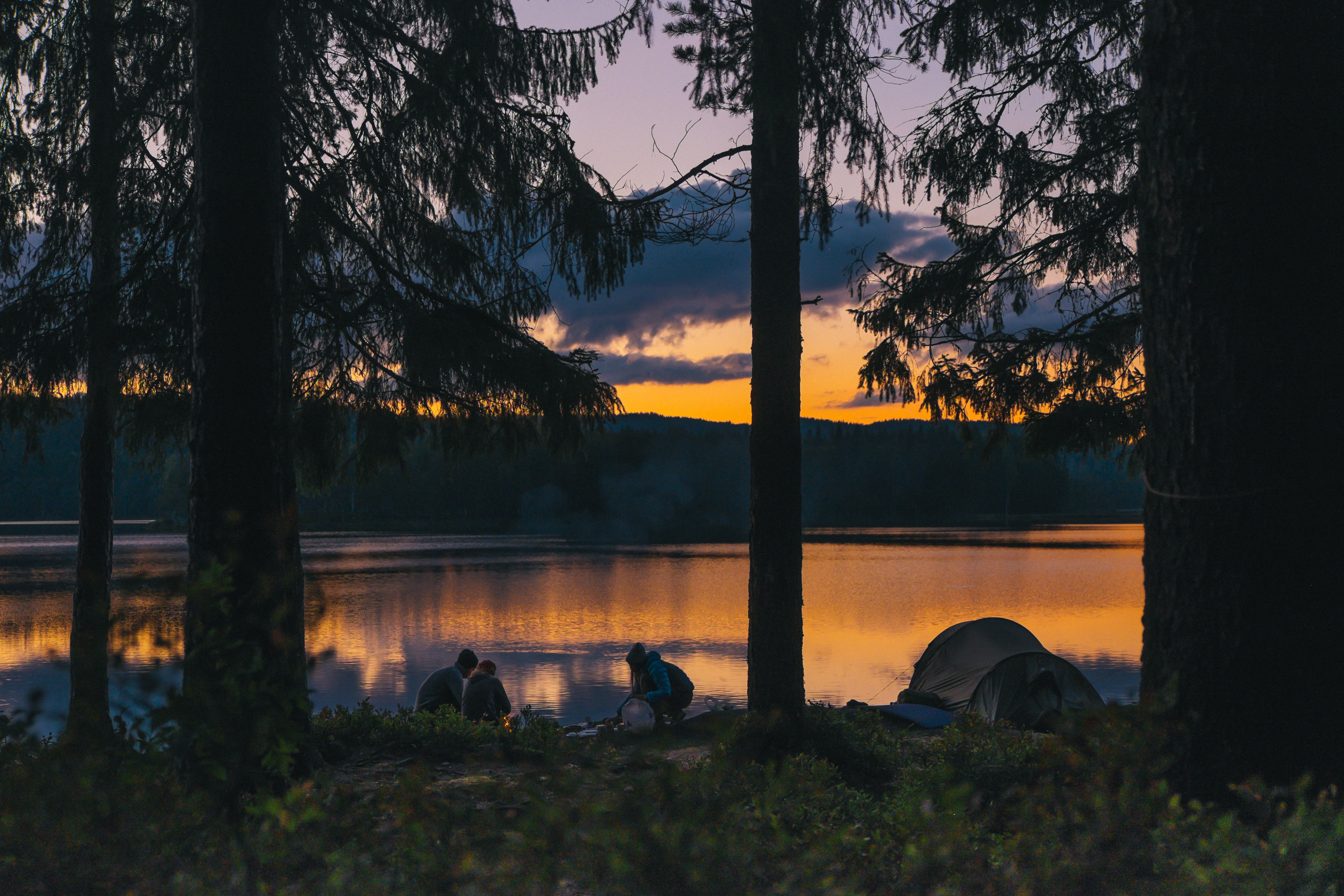 Camping by a lake at sunset with tents and people HD Wallpaper