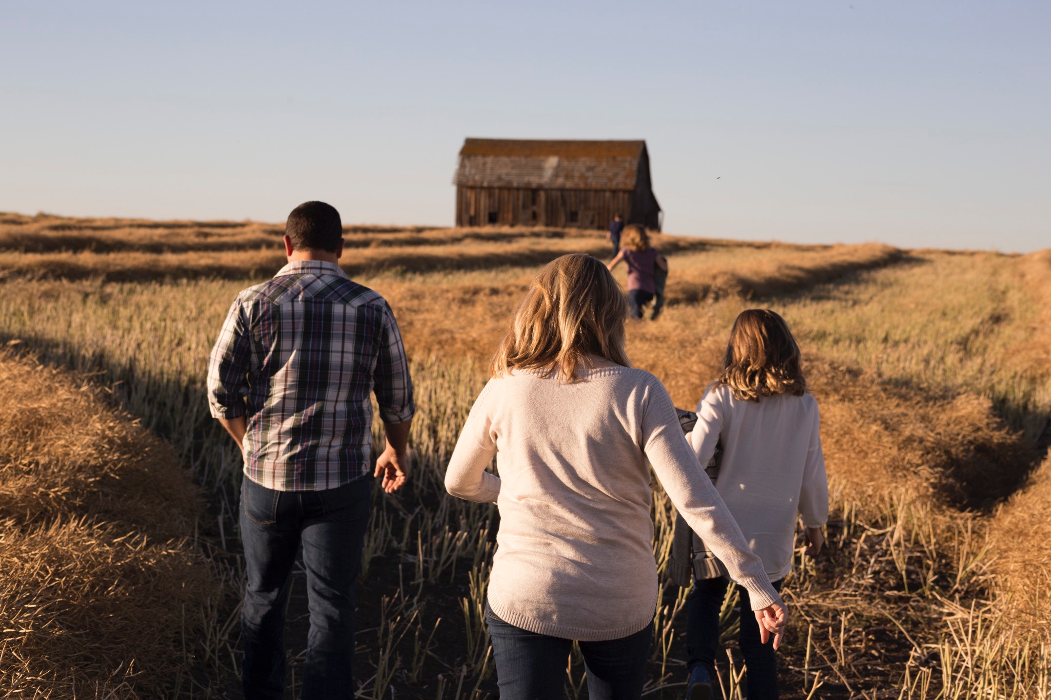 Family walks through a field towards a barn HD Wallpaper
