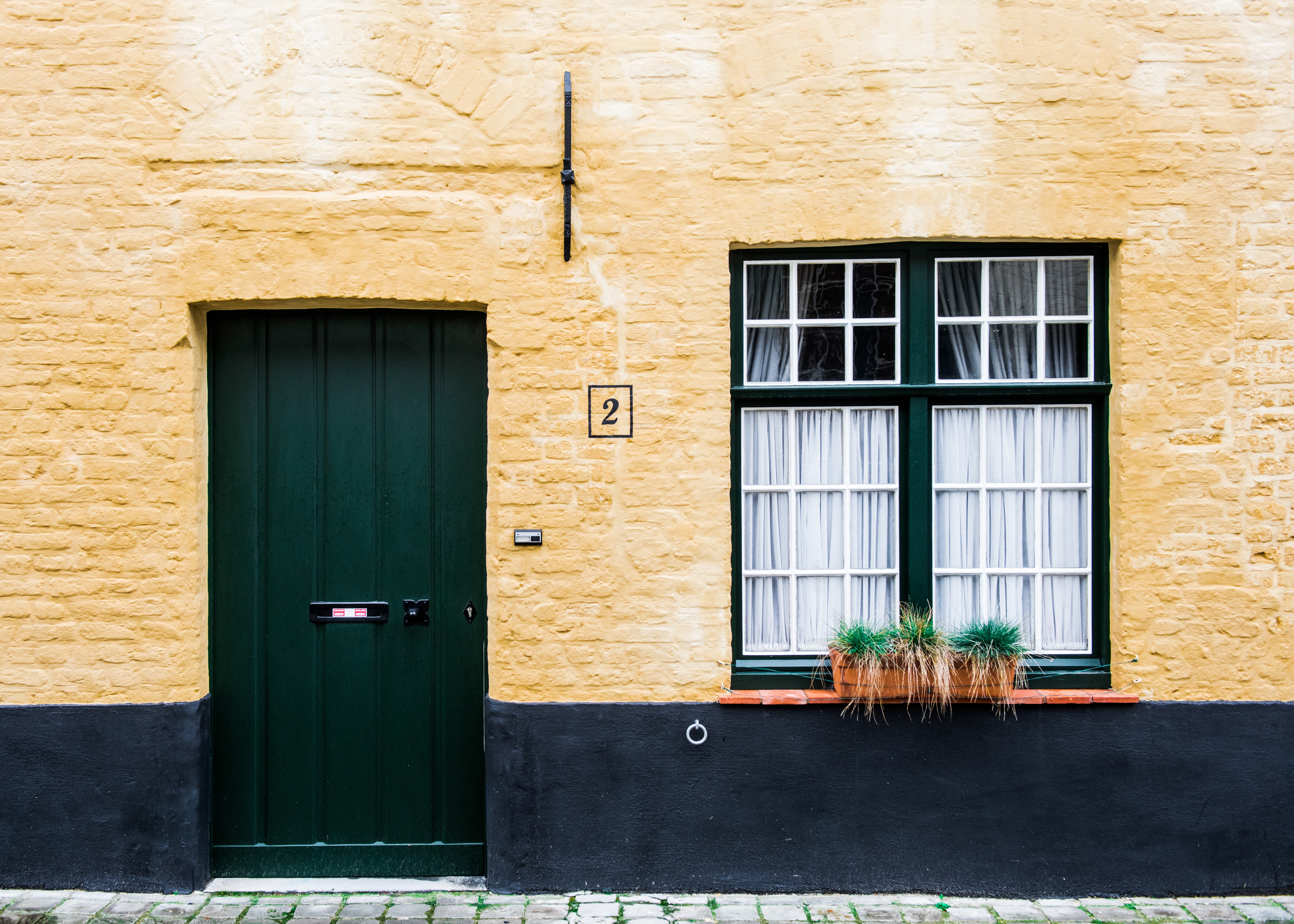 Yellow brick house with green door and window HD Wallpaper