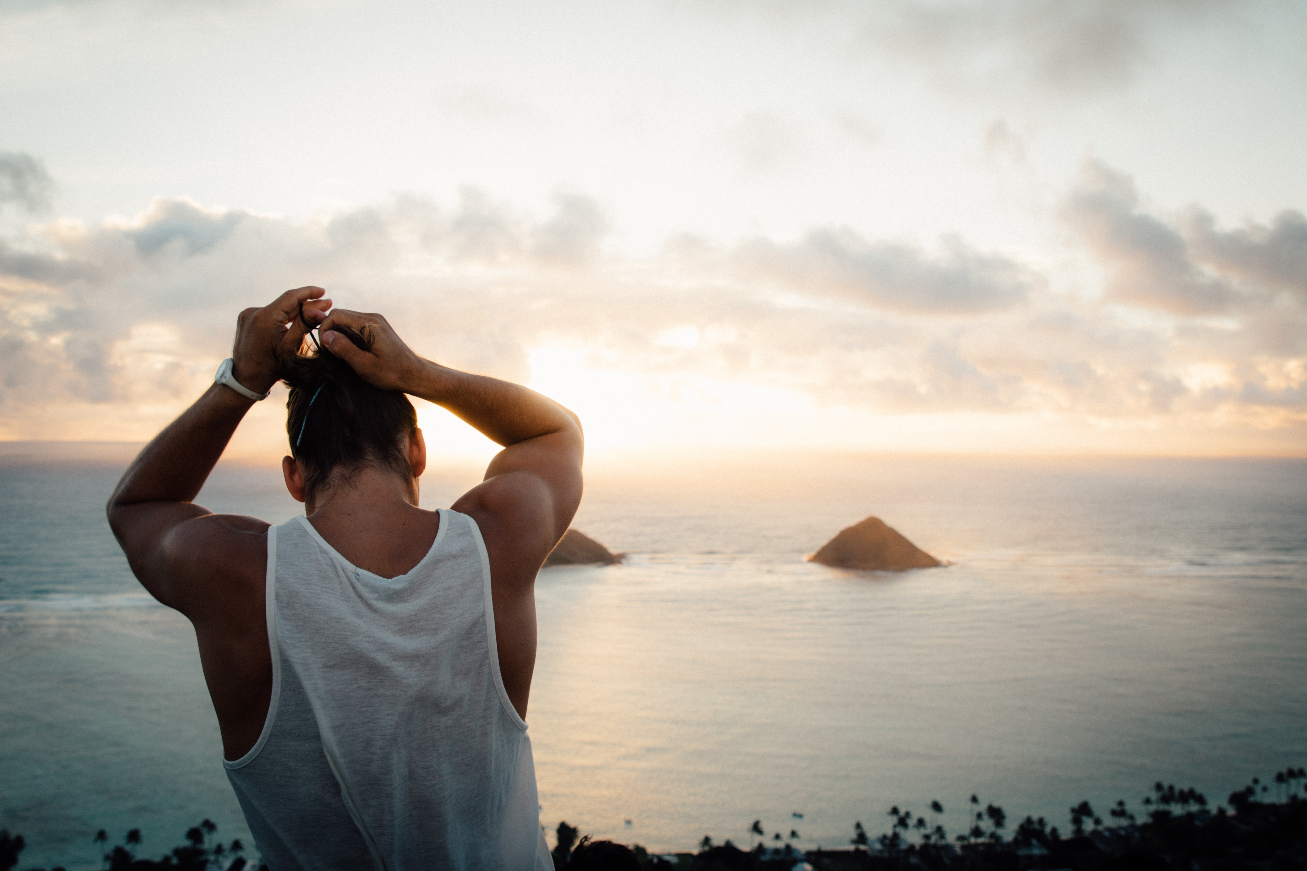 Man tying hair at sunset overlooking ocean with islands HD Wallpaper