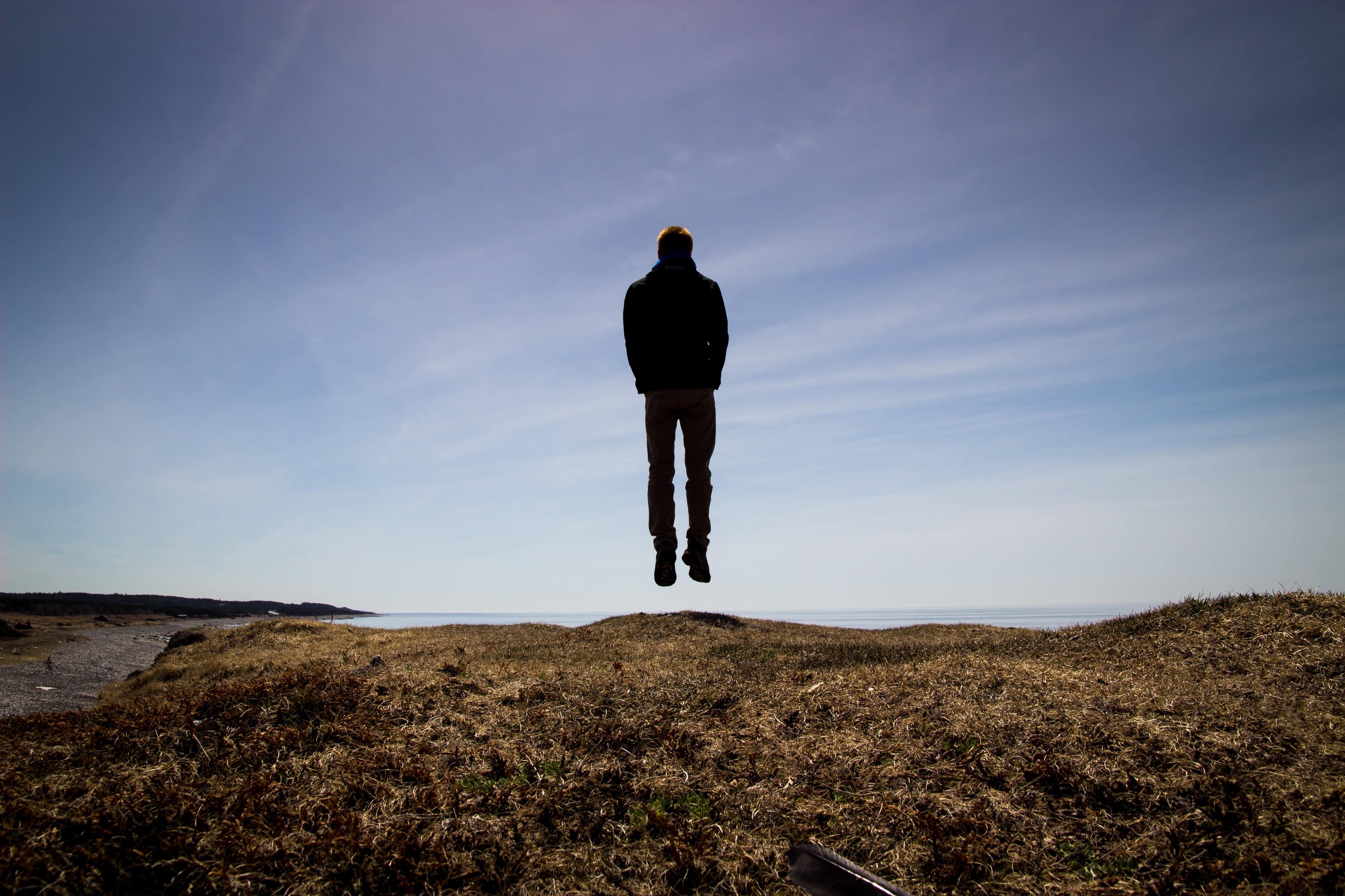 Man levitating over a grassy cliff by the ocean HD Wallpaper