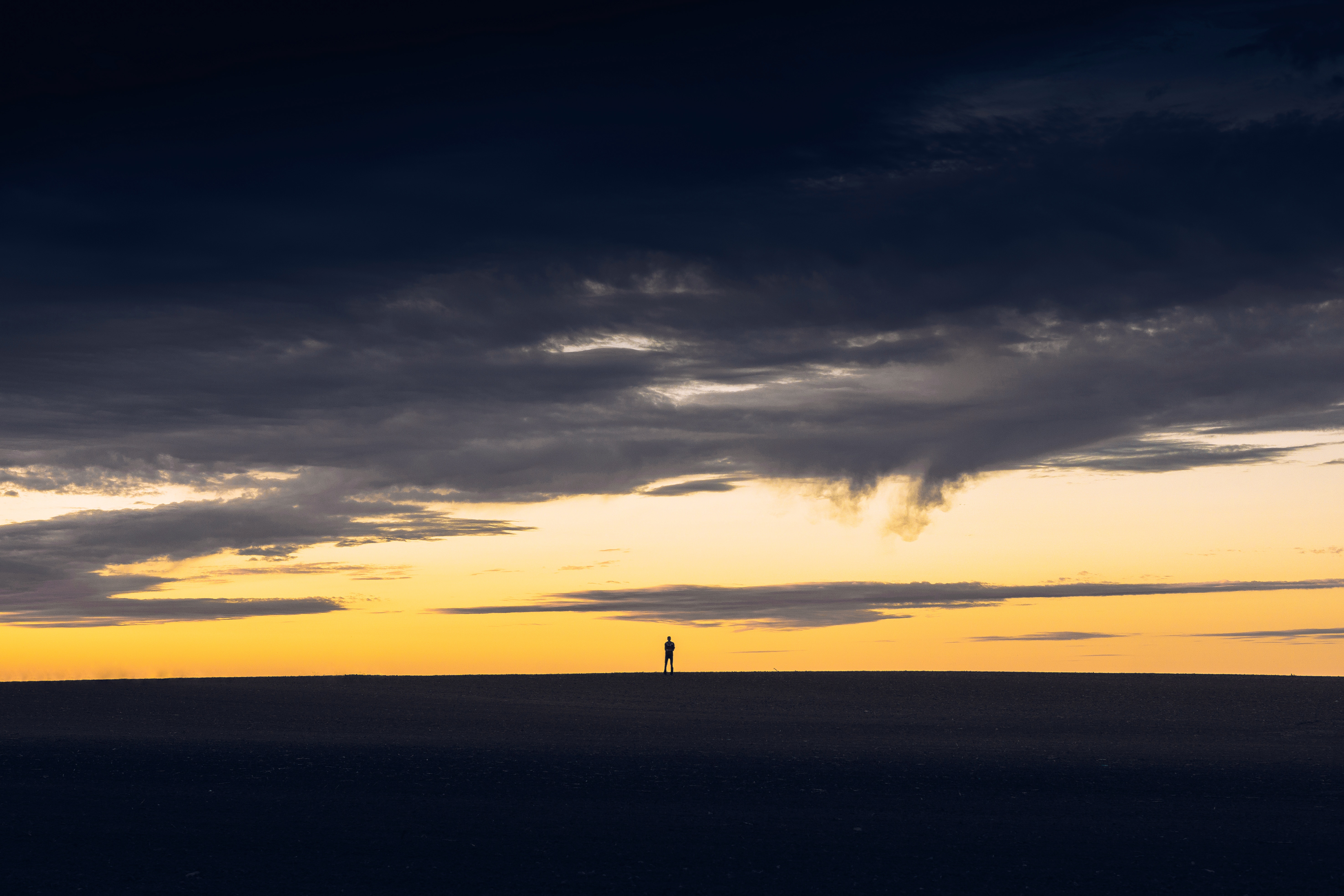 Silhouette of a person on a barren horizon at sunset HD Wallpaper