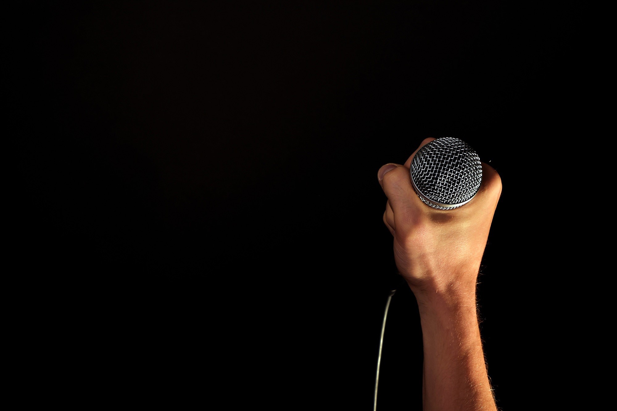 Hand holding a microphone against a black background HD Wallpaper