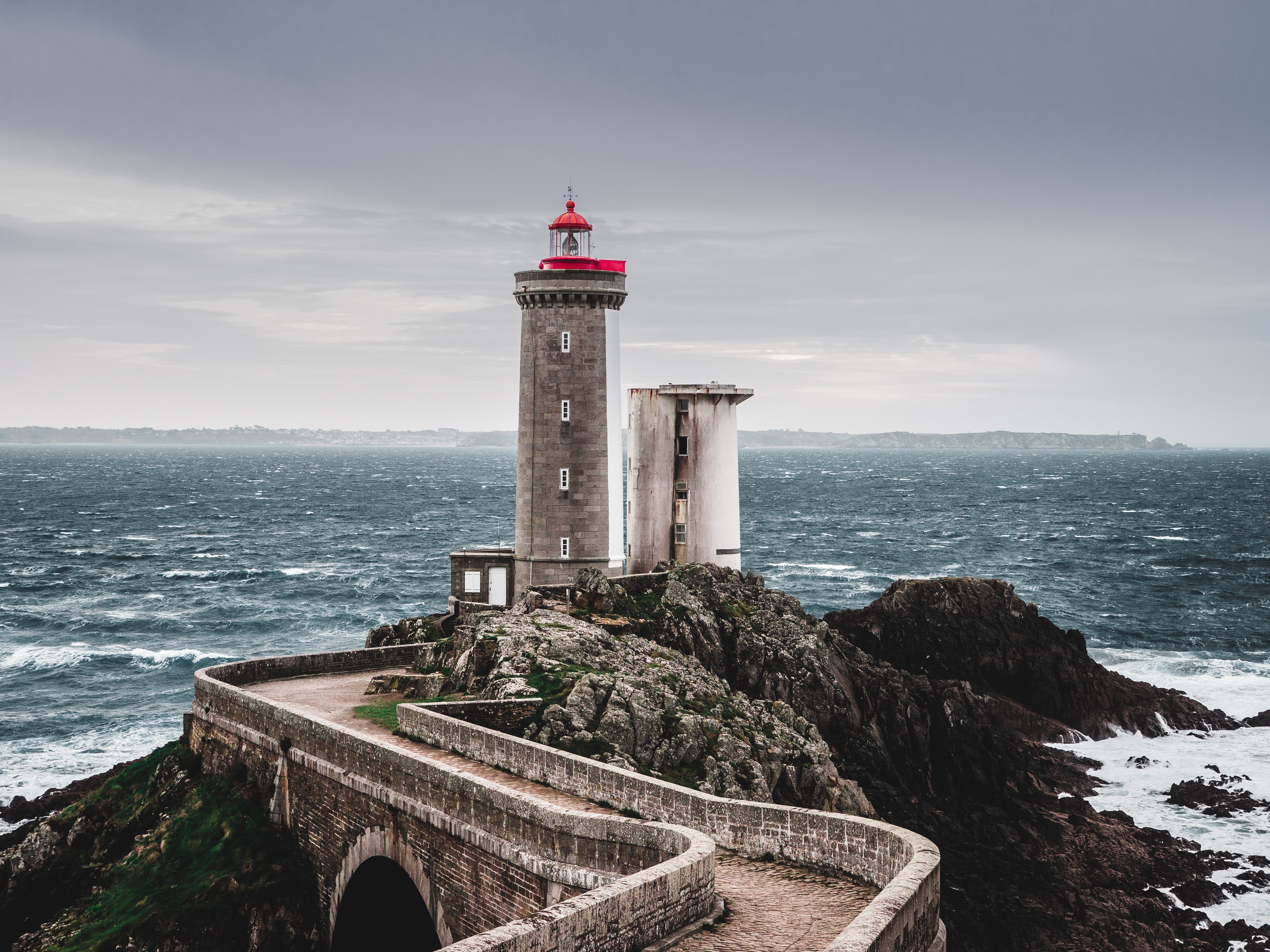 Lighthouse on a rocky coast with a stone path HD Wallpaper