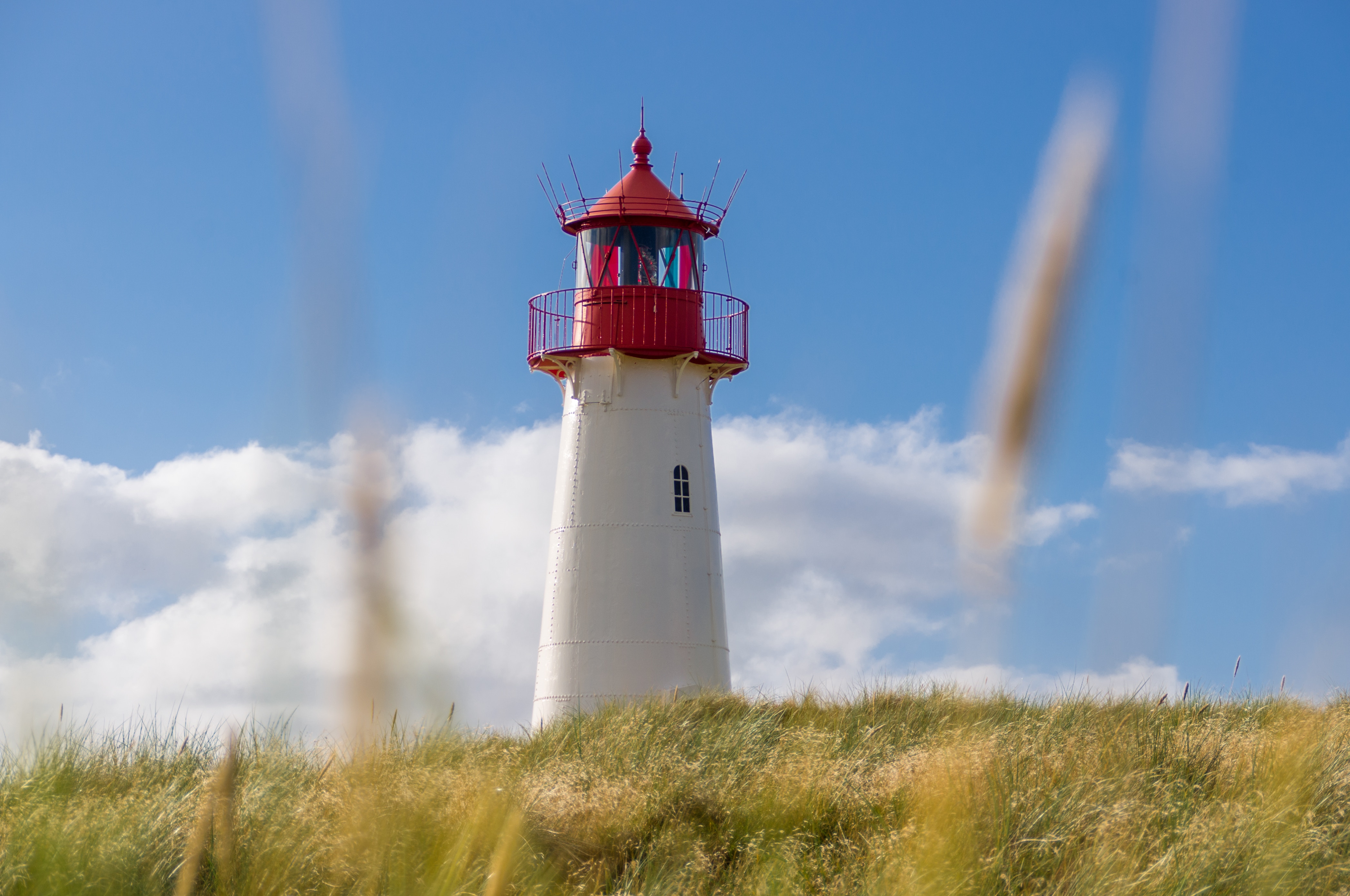 White lighthouse with red top on grassy hill HD Wallpaper