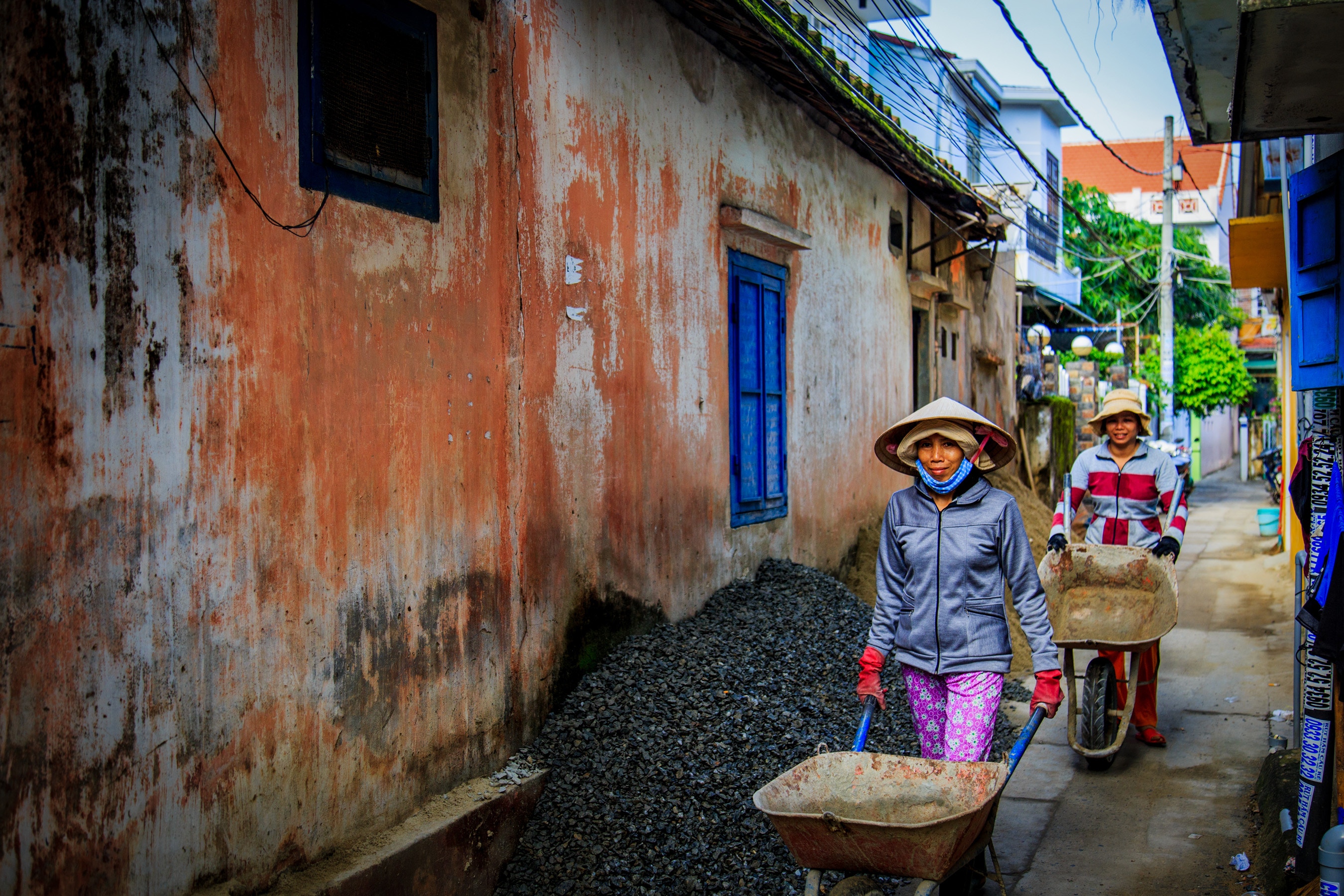 Two women with conical hats pushing wheelbarrows in Hoi An HD Wallpaper