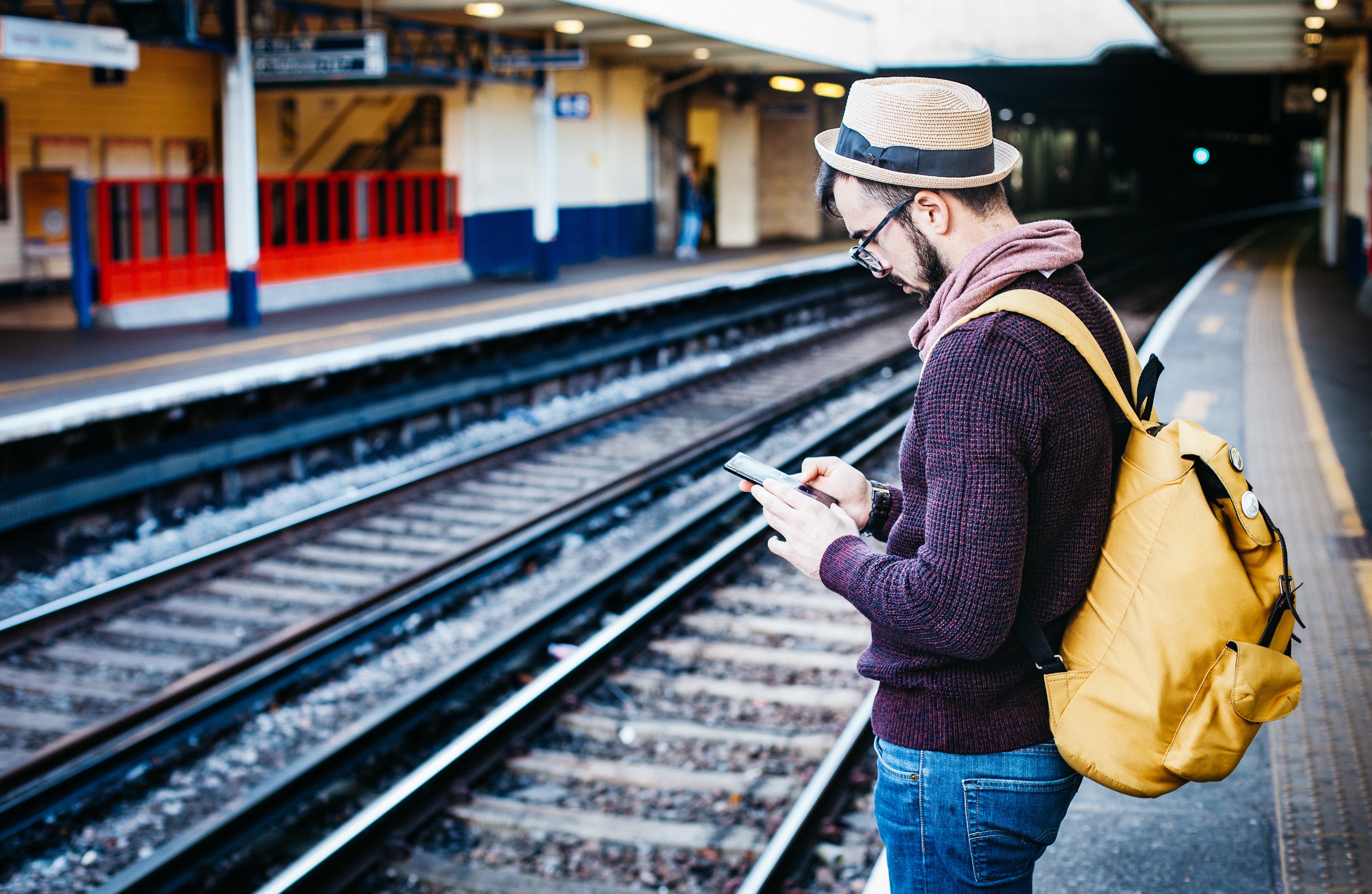 Man with backpack using smartphone at train station HD Wallpaper