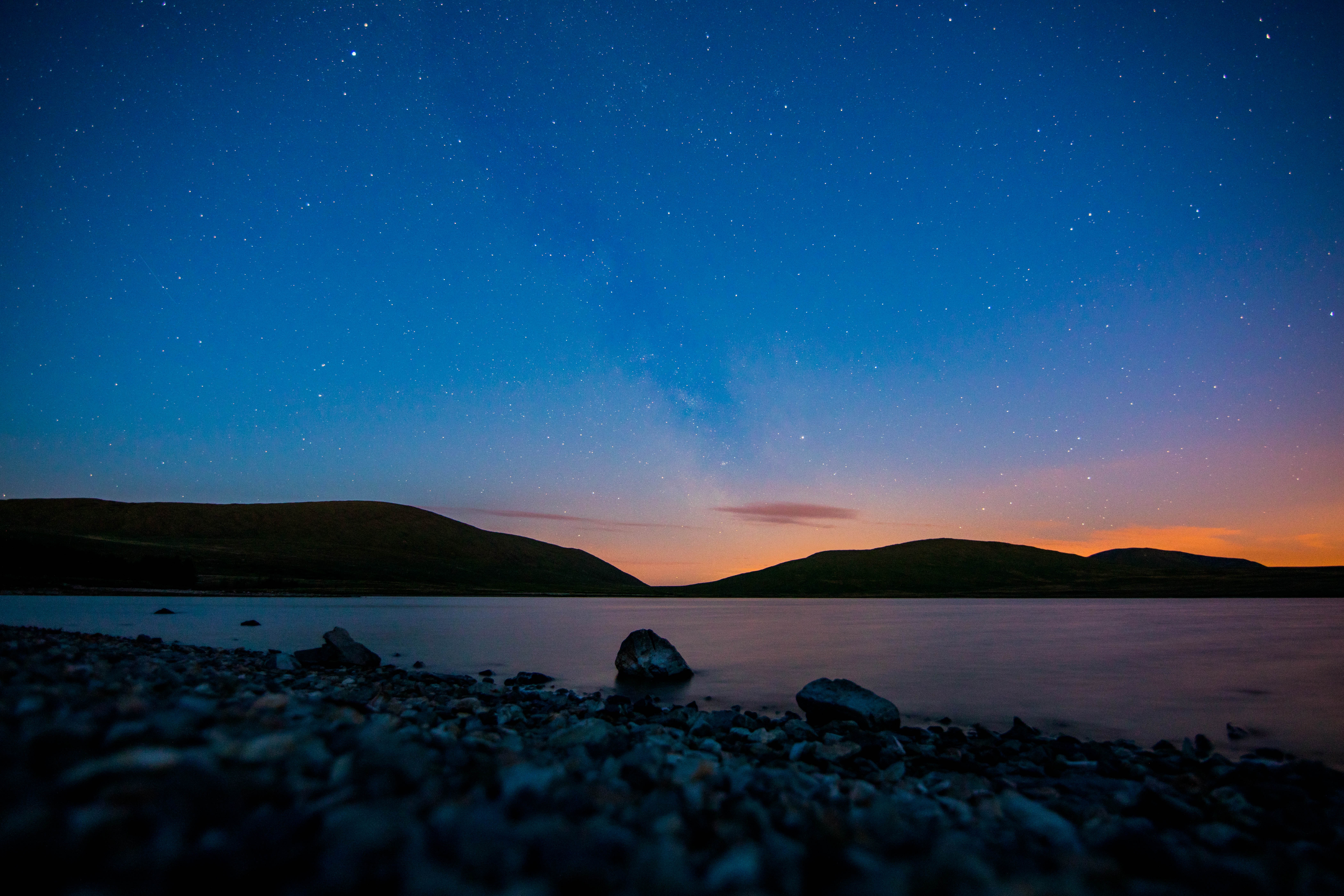 Night sky over a lake with stars and hills HD Wallpaper