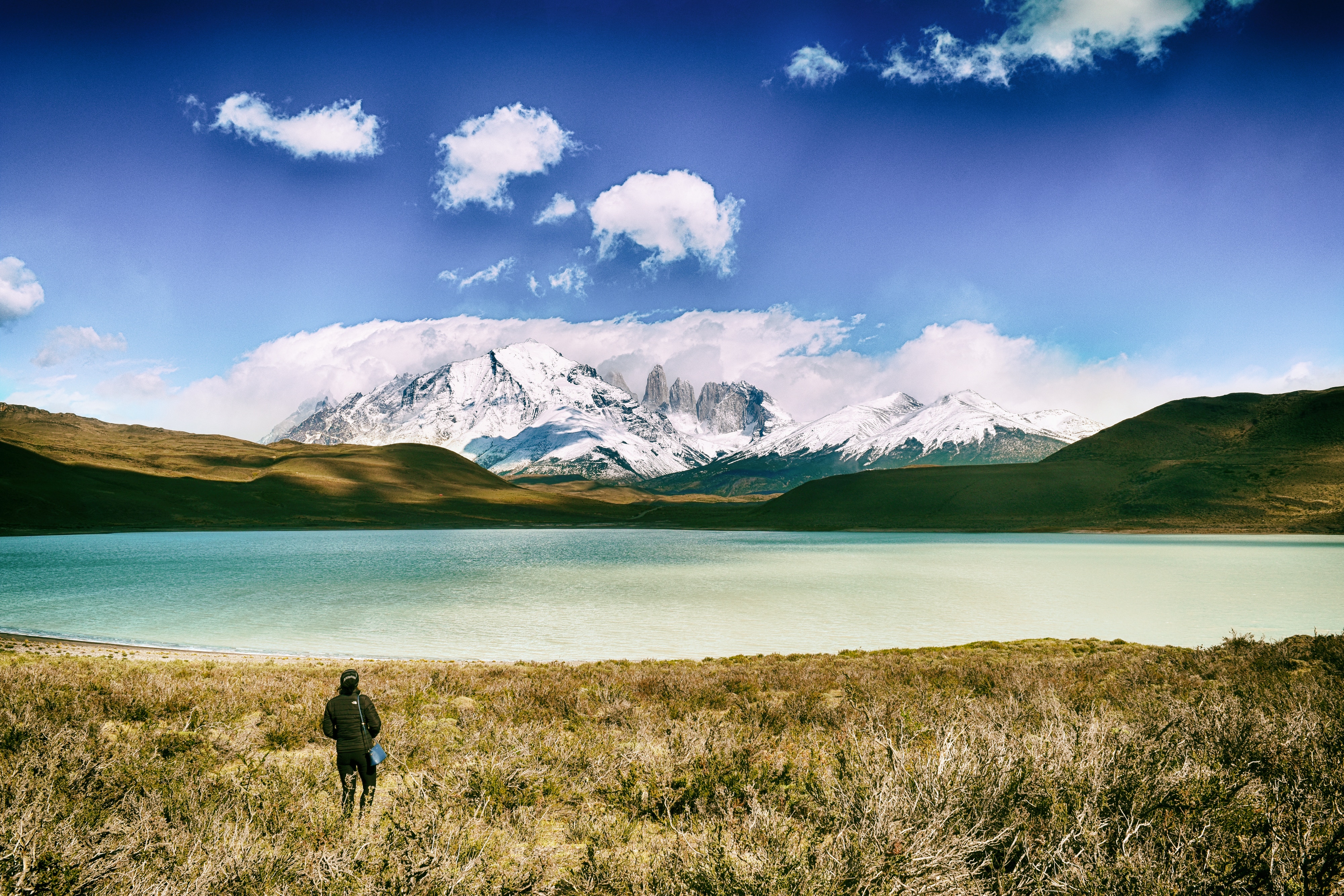 Person walking towards snowy mountains and lake HD Wallpaper