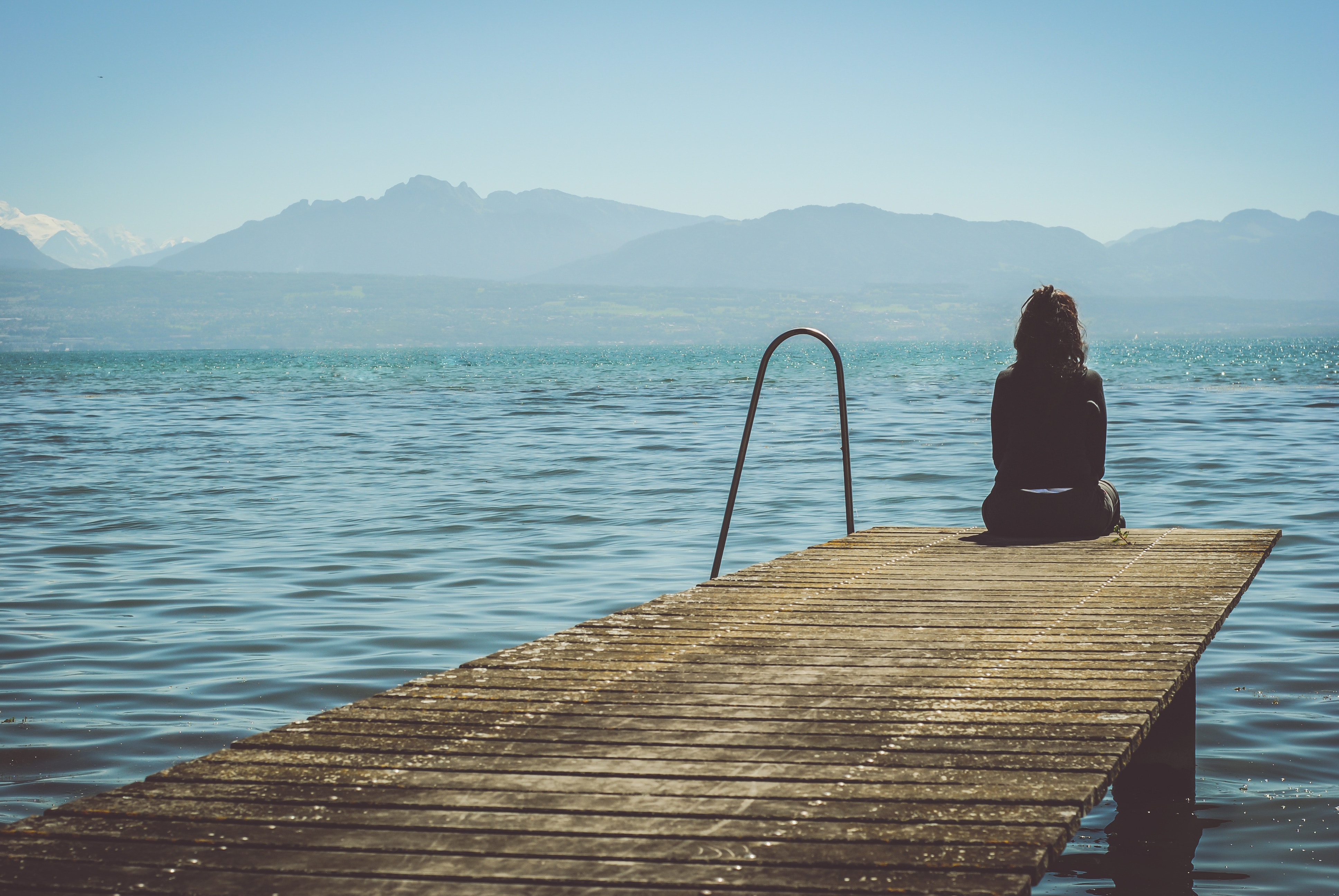 Woman sitting on a wooden dock overlooking mountains HD Wallpaper