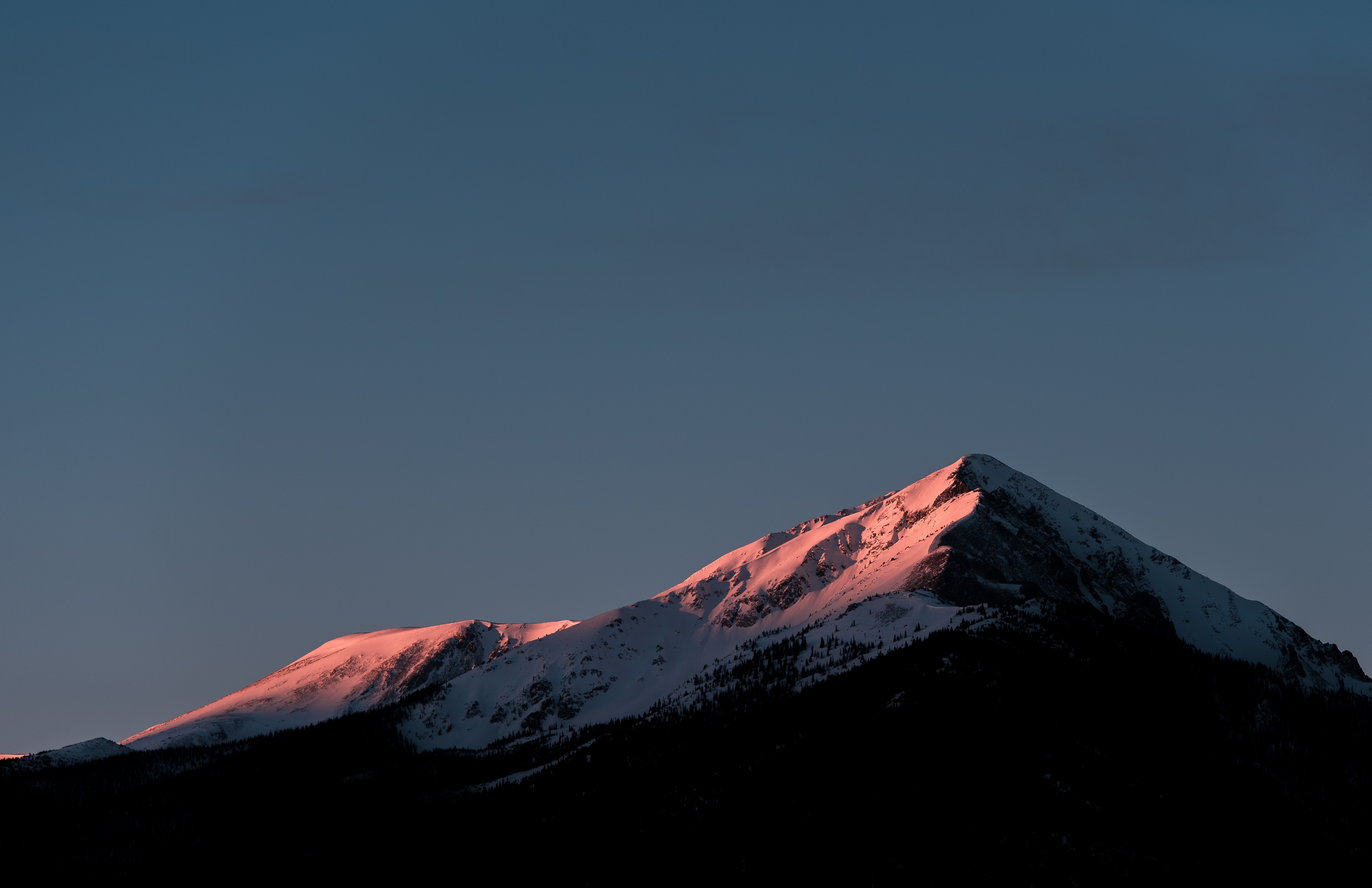 Snowy mountain peak illuminated by sunrise glow HD Wallpaper