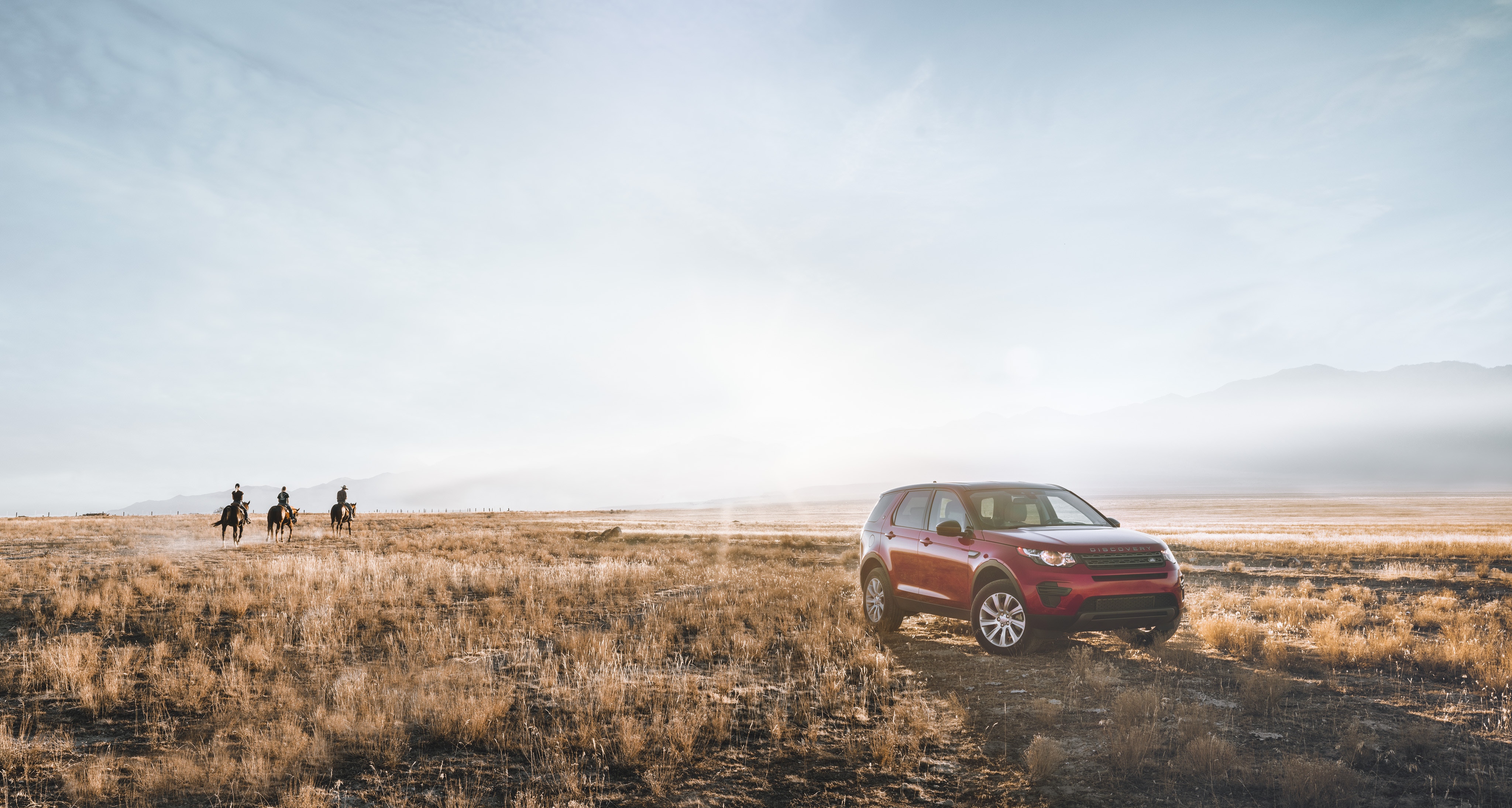 Red Land Rover Discovery Sport in a Field with Horse Riders HD Wallpaper