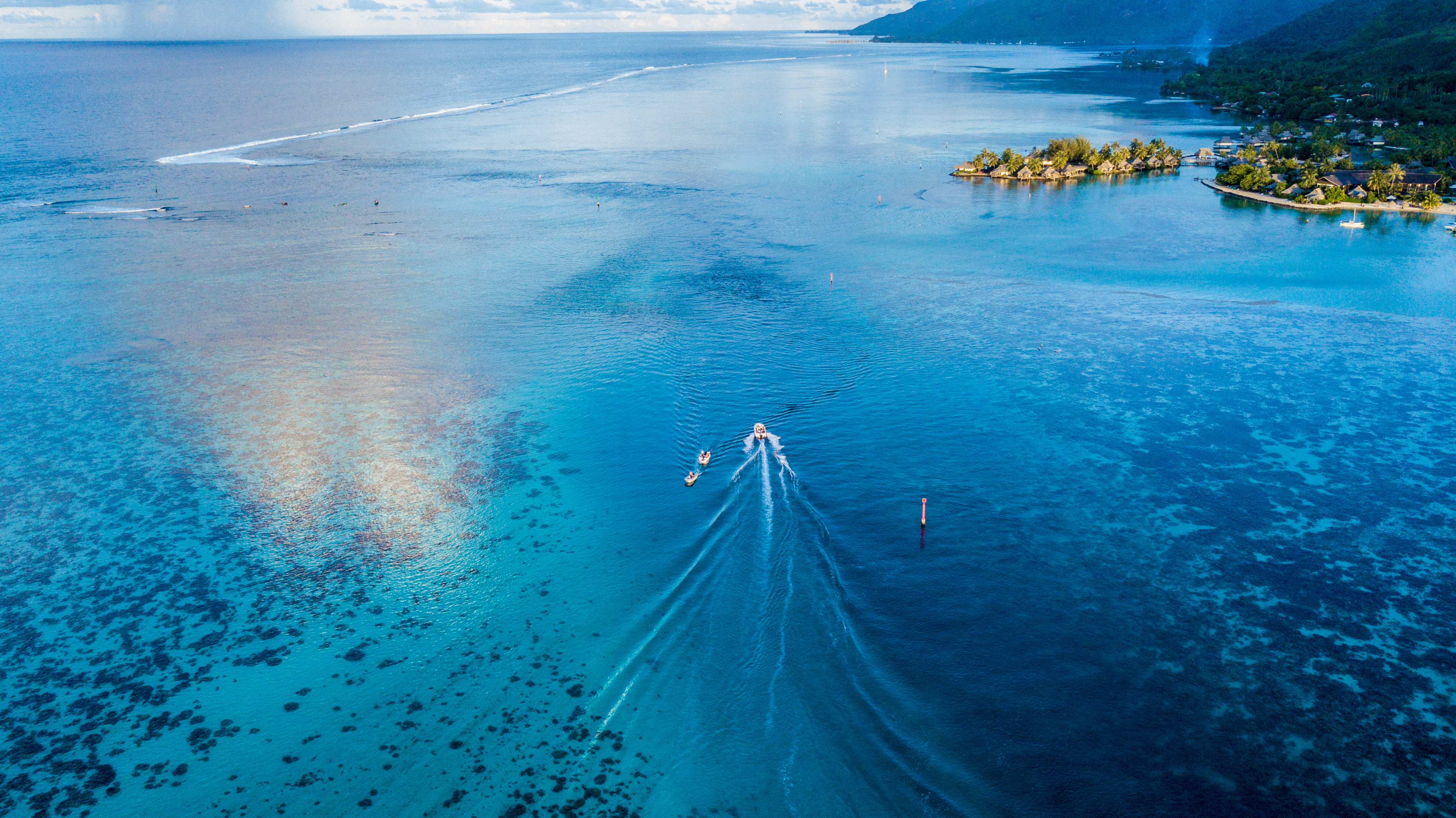 Boat sailing in a clear blue ocean near a tropical island HD Wallpaper