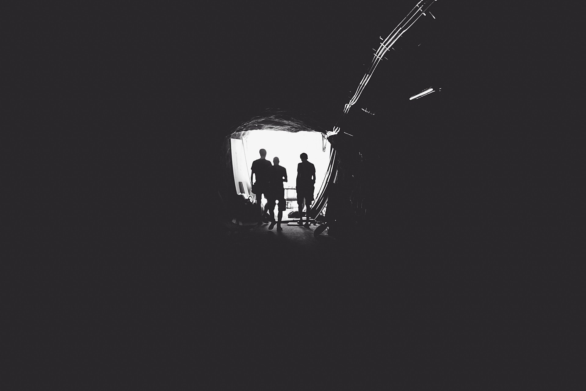 Silhouettes of people in a dark tunnel with light ahead HD Wallpaper
