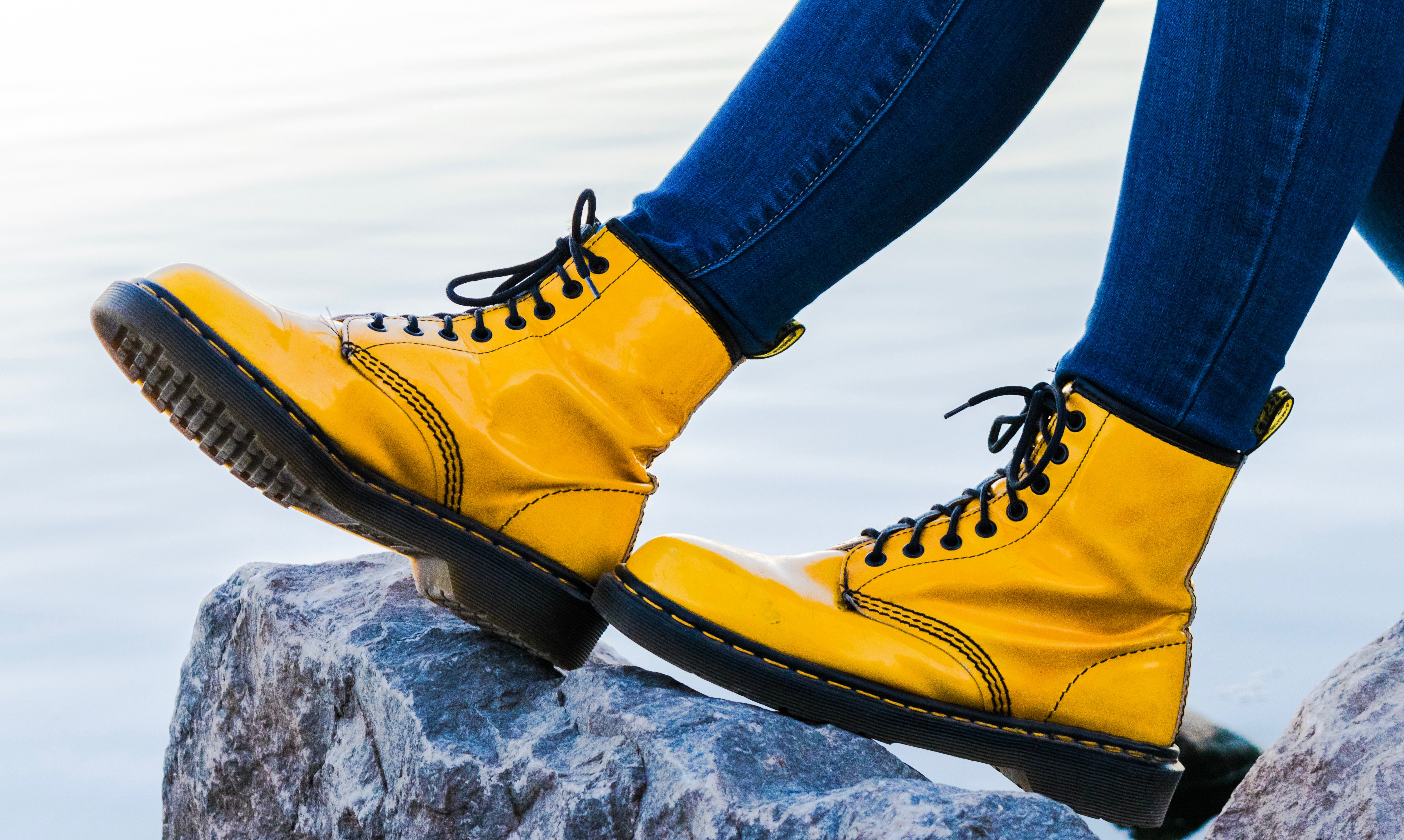 Yellow Dr. Martens boots on rocks near water HD Wallpaper