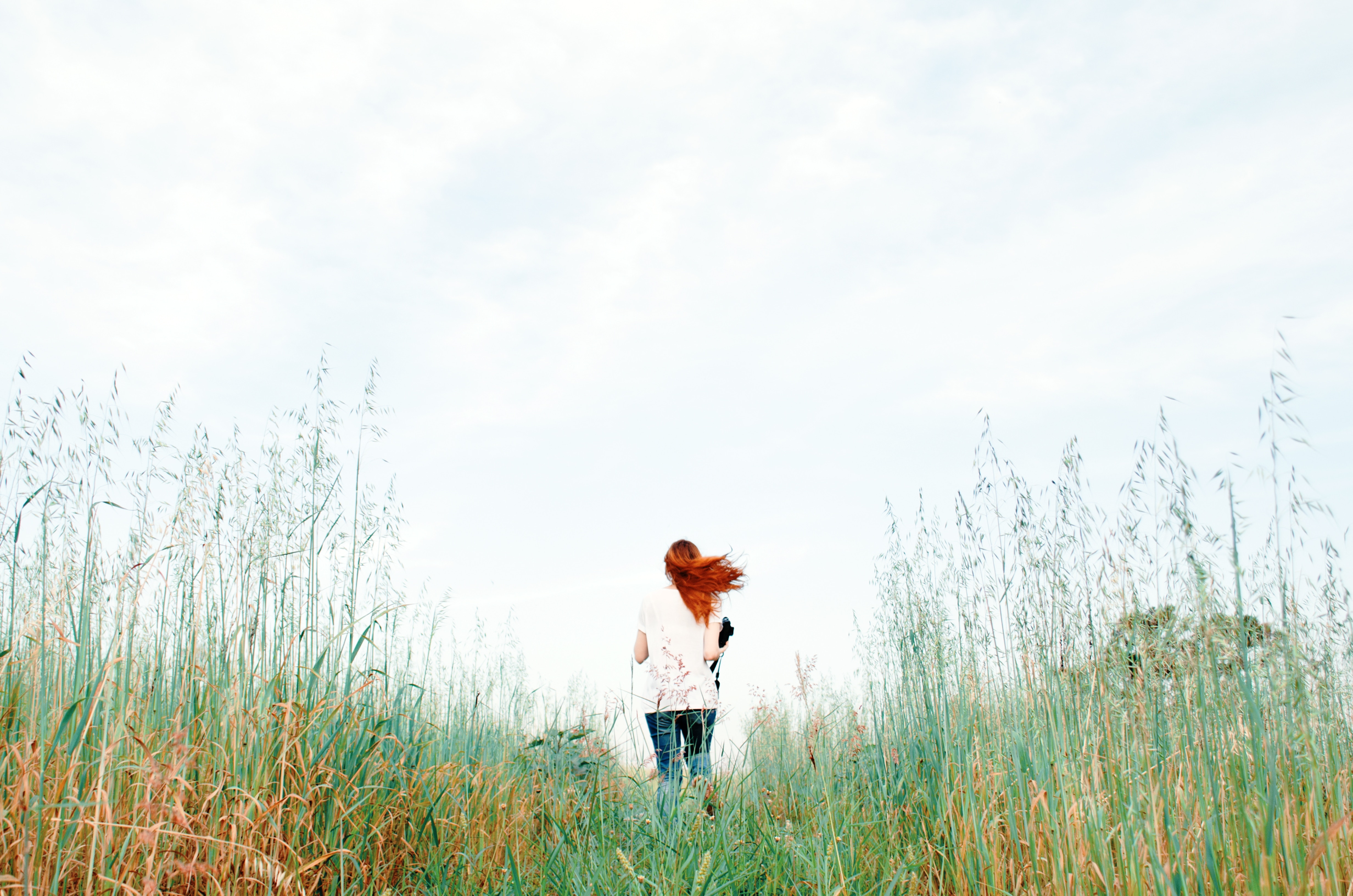 Woman with red hair walking through a grassy field HD Wallpaper