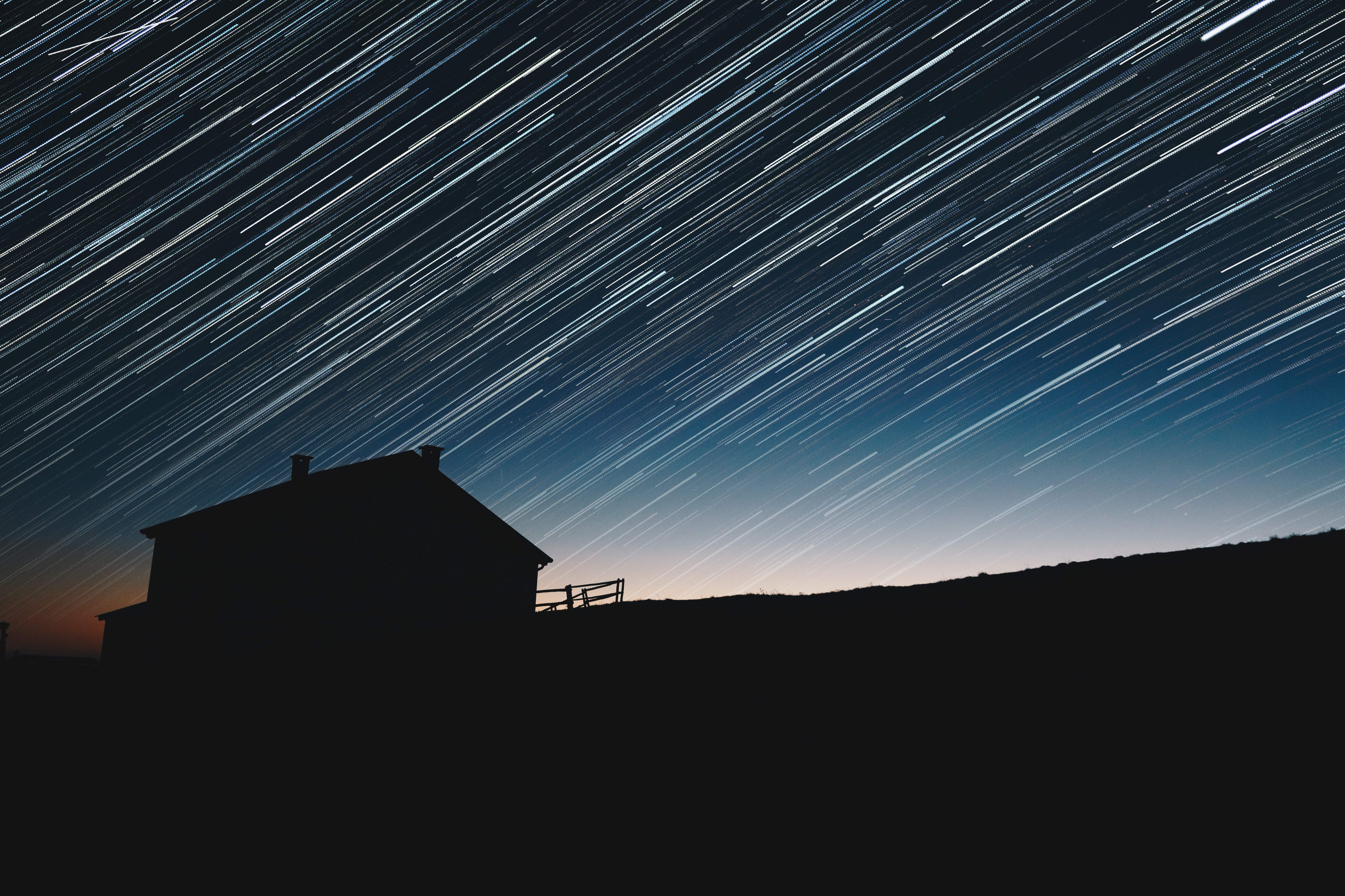 Silhouette of a house under star trails HD Wallpaper