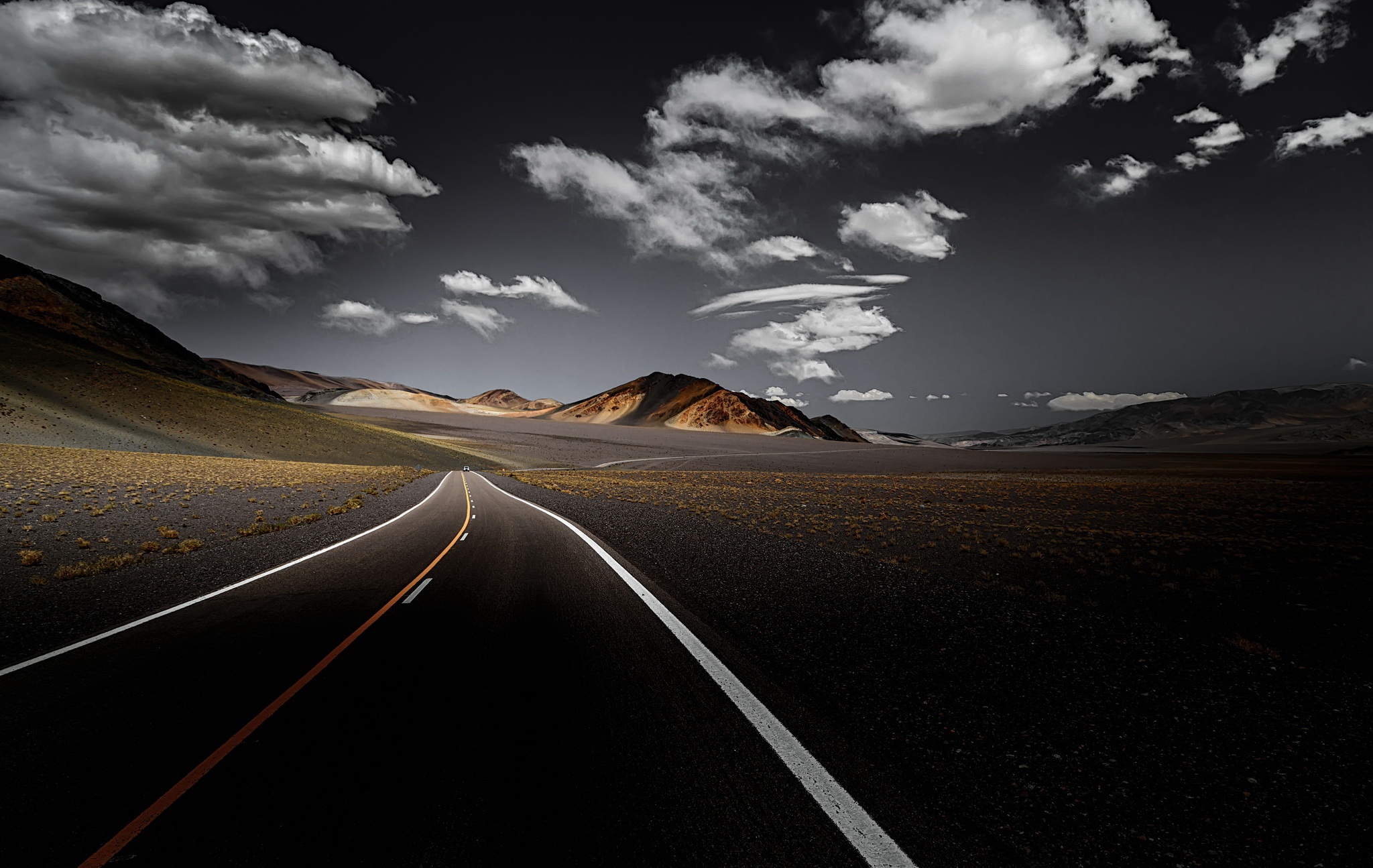 Road through a desolate landscape with mountains and clouds HD Wallpaper