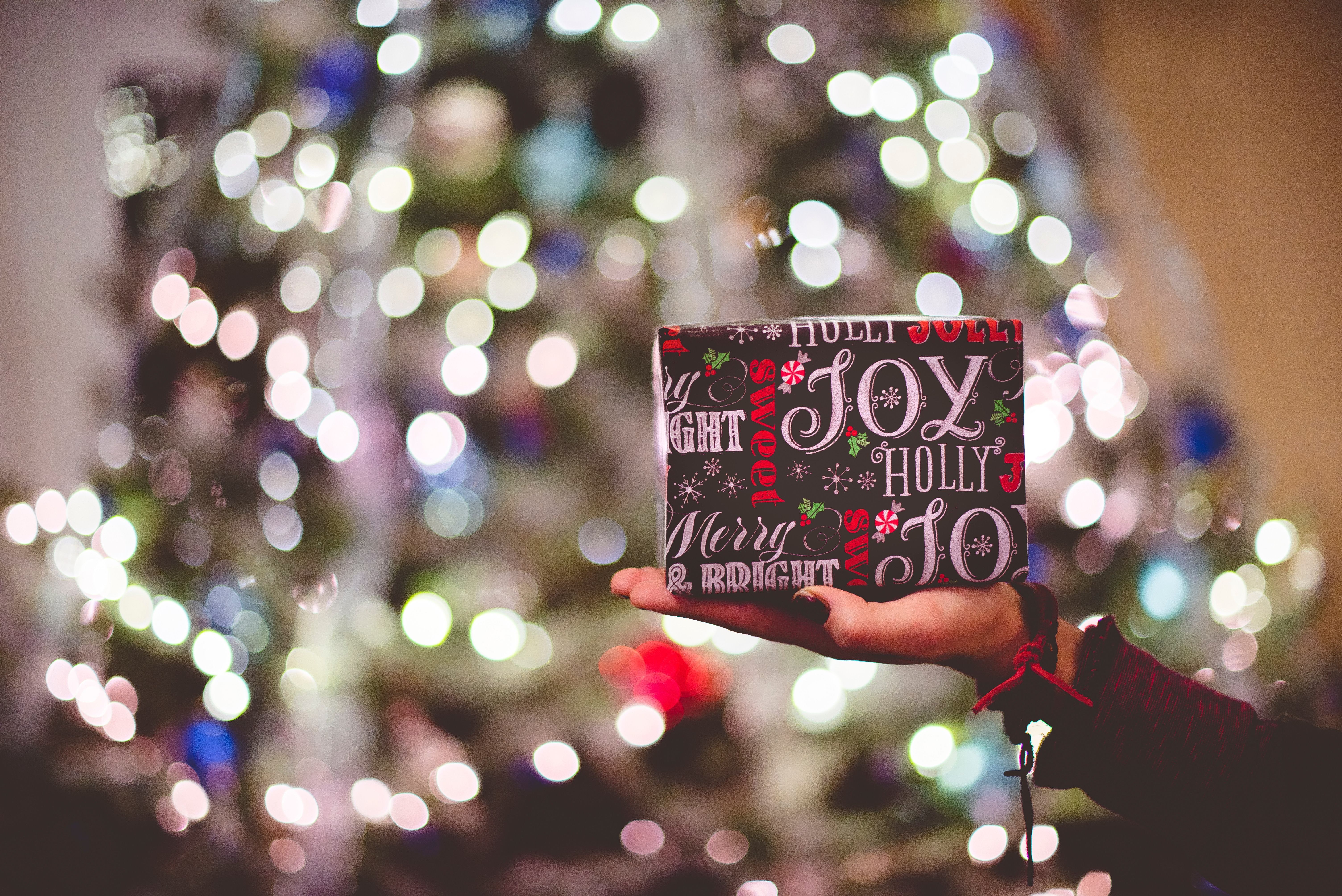 Hand holding a Christmas gift in front of a bokeh tree HD Wallpaper