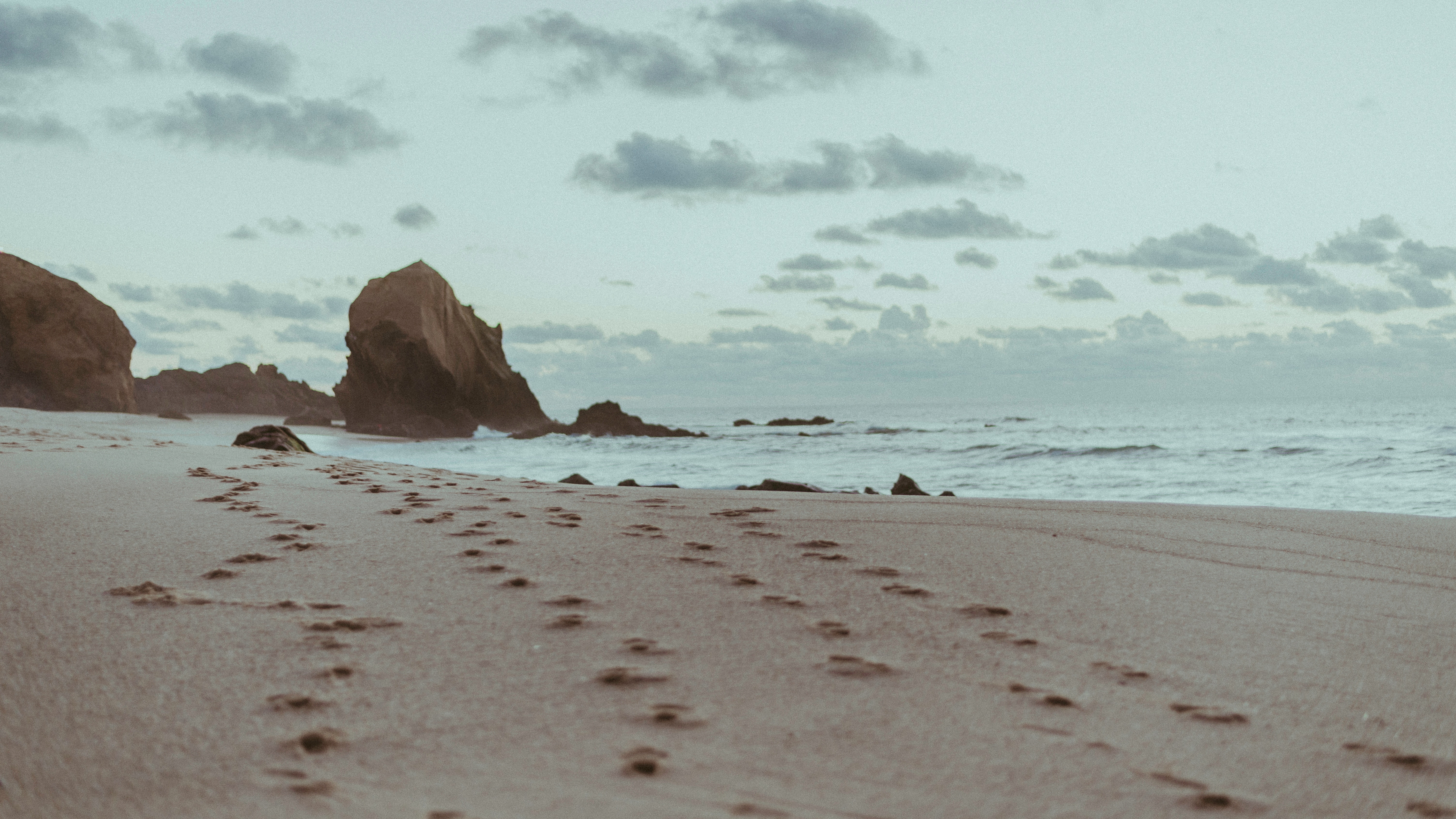 Footprints on a sandy beach with ocean and rocks HD Wallpaper
