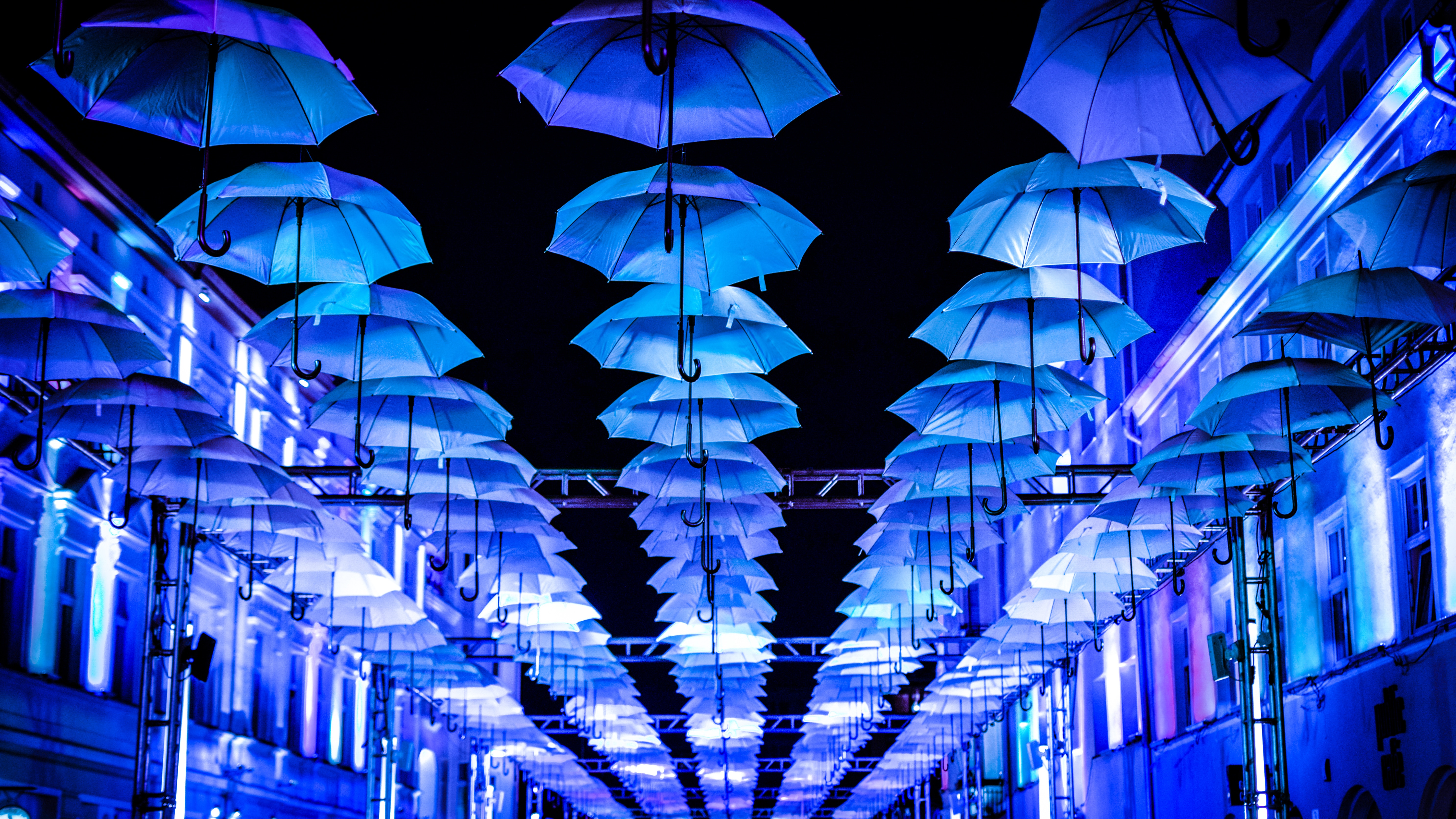Blue umbrellas illuminated at night above a street HD Wallpaper