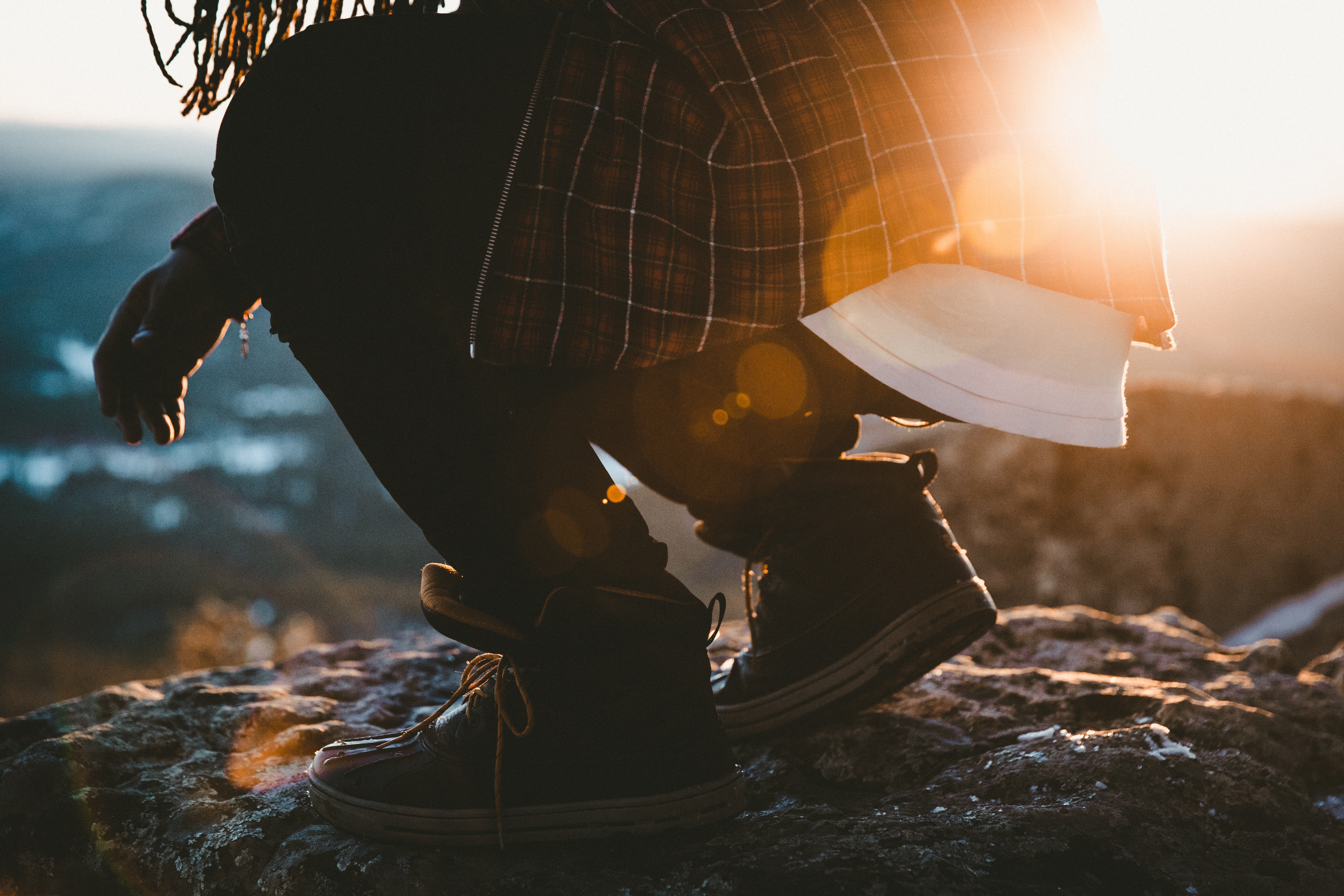 Person in plaid shirt crouching on rock at sunset HD Wallpaper