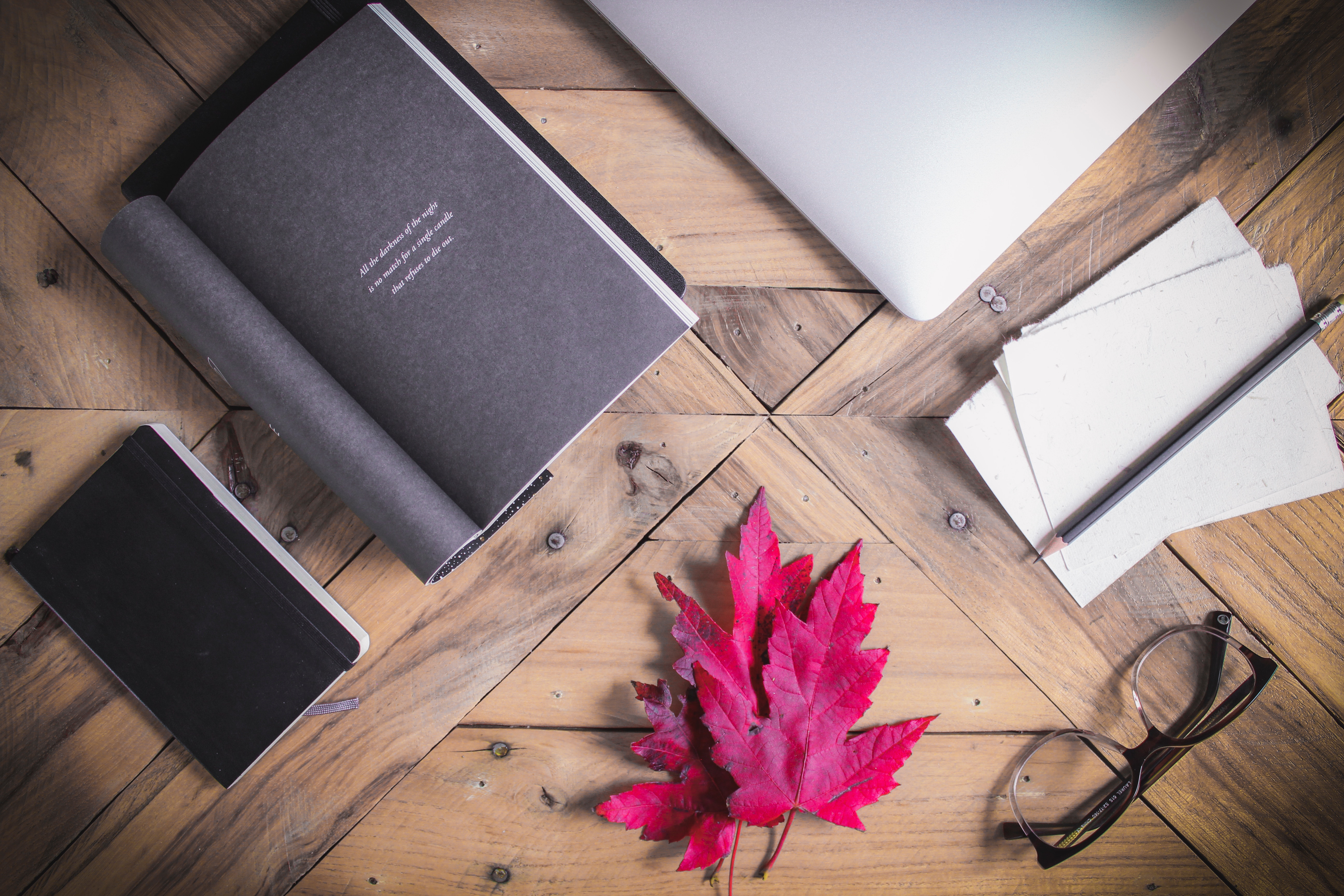 Flat lay of a laptop, books, glasses, and a red maple leaf on a wooden table HD Wallpaper