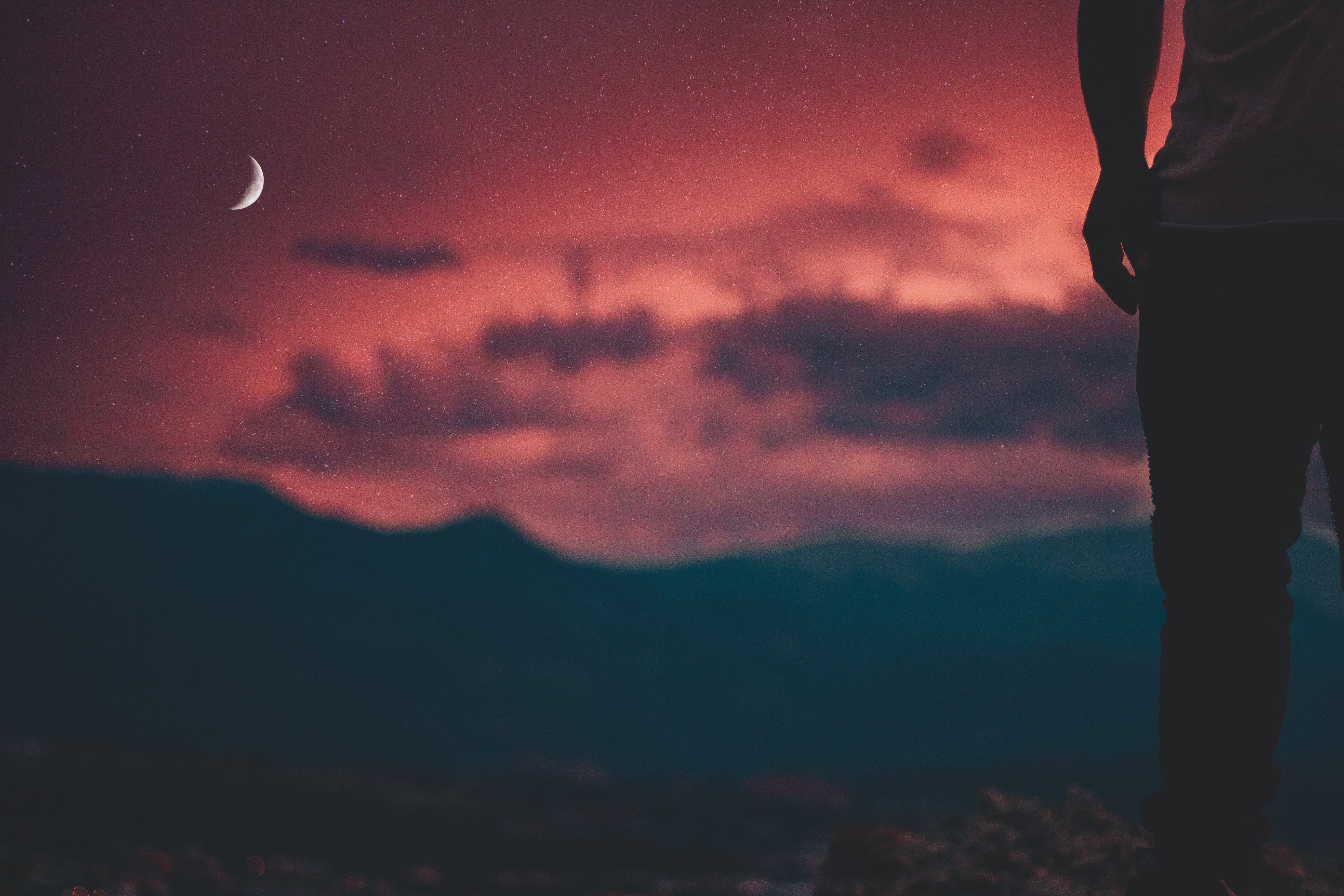Silhouette of a person against a red sky with moon and mountains HD Wallpaper