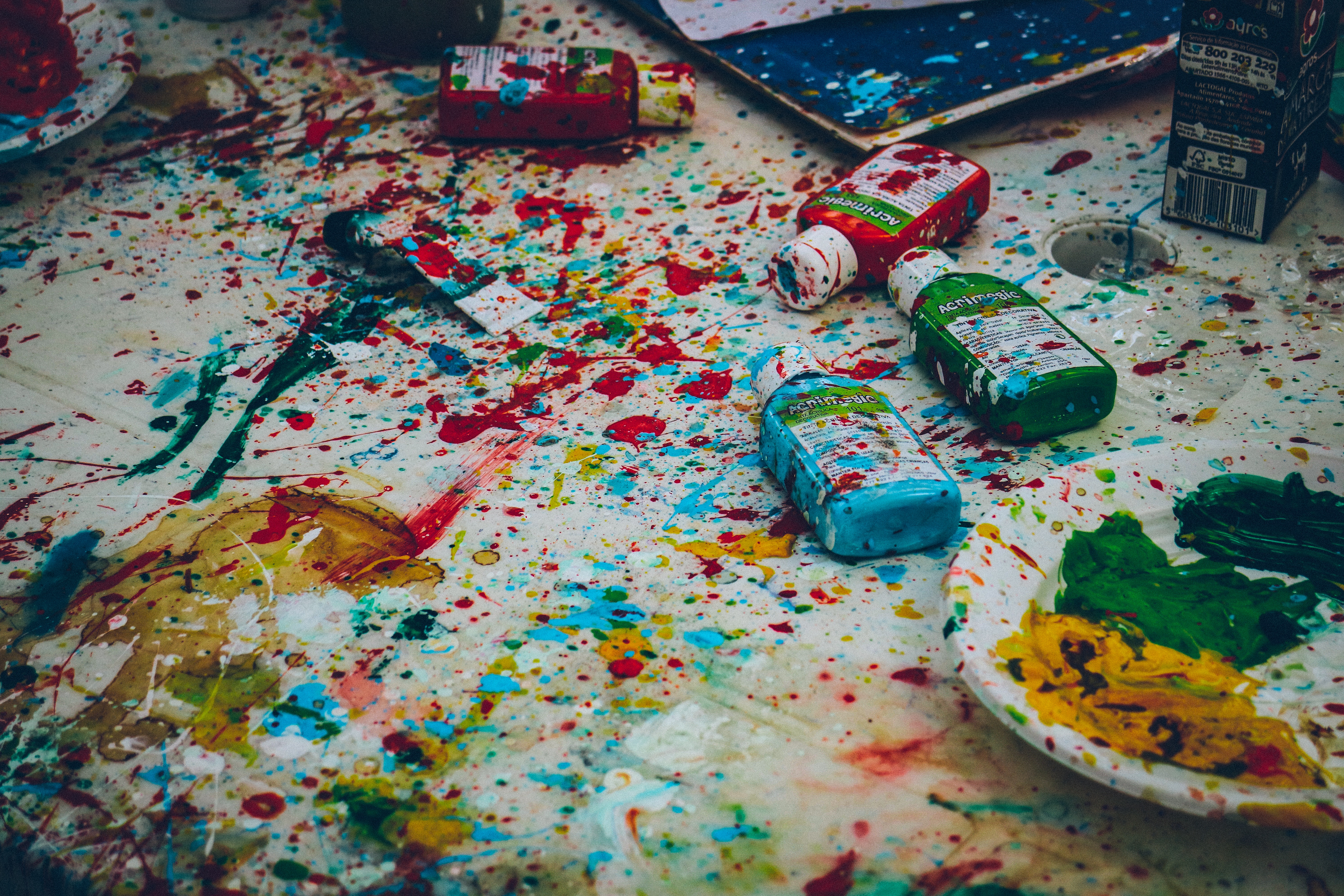 Messy art table with paint bottles and splatters HD Wallpaper
