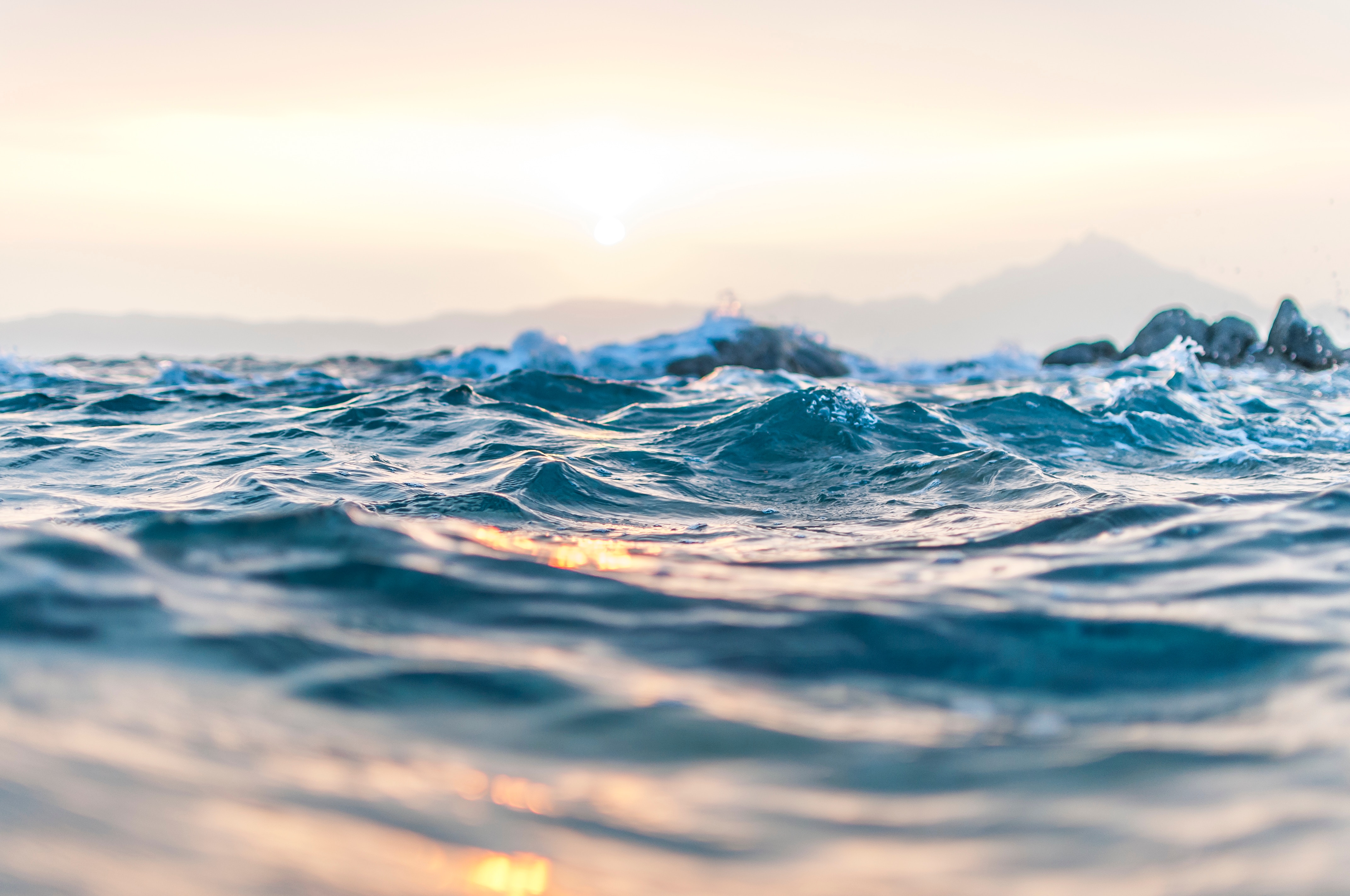 Ocean waves at sunrise with distant mountains HD Wallpaper