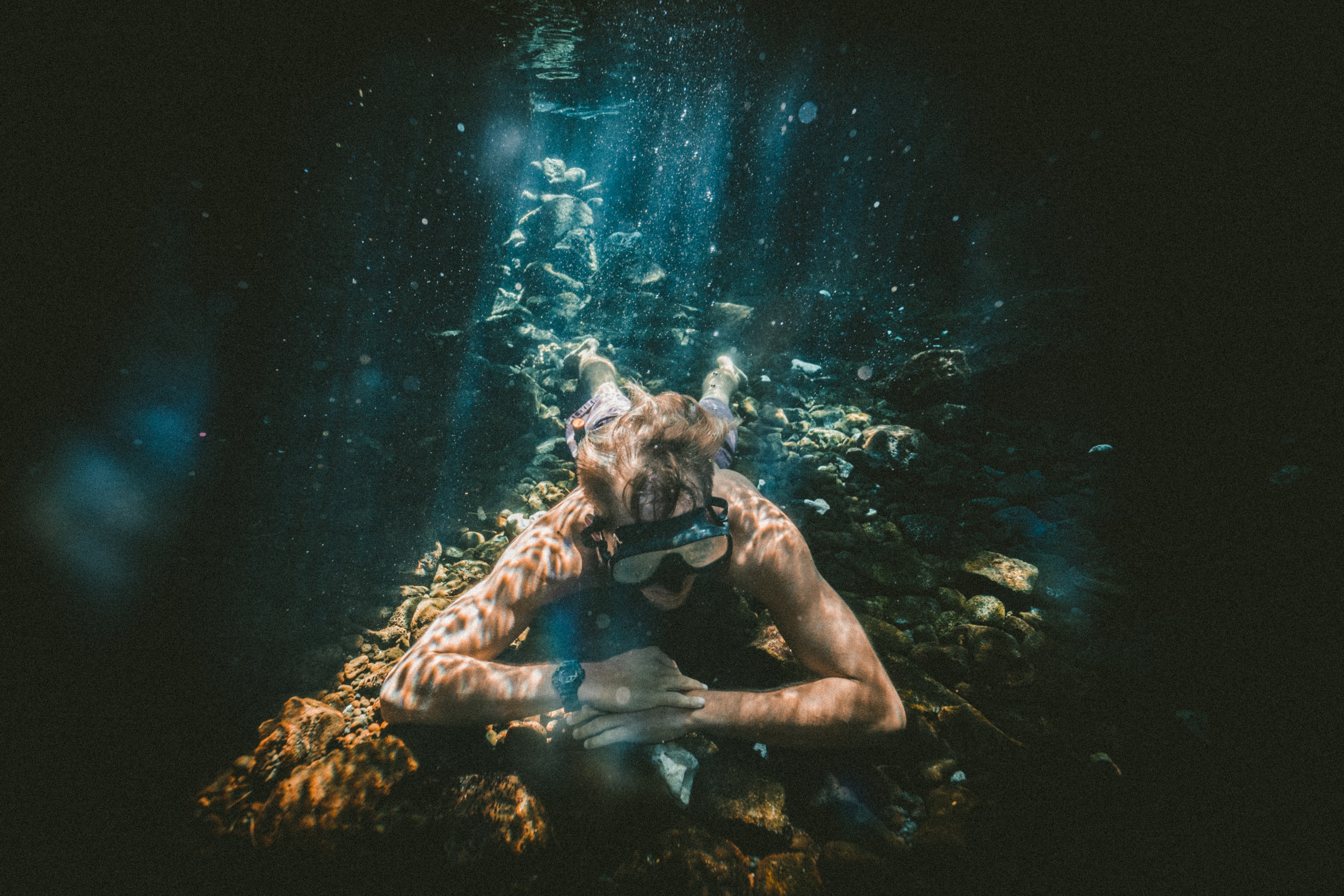 Underwater diver resting on rocks with sunbeams HD Wallpaper