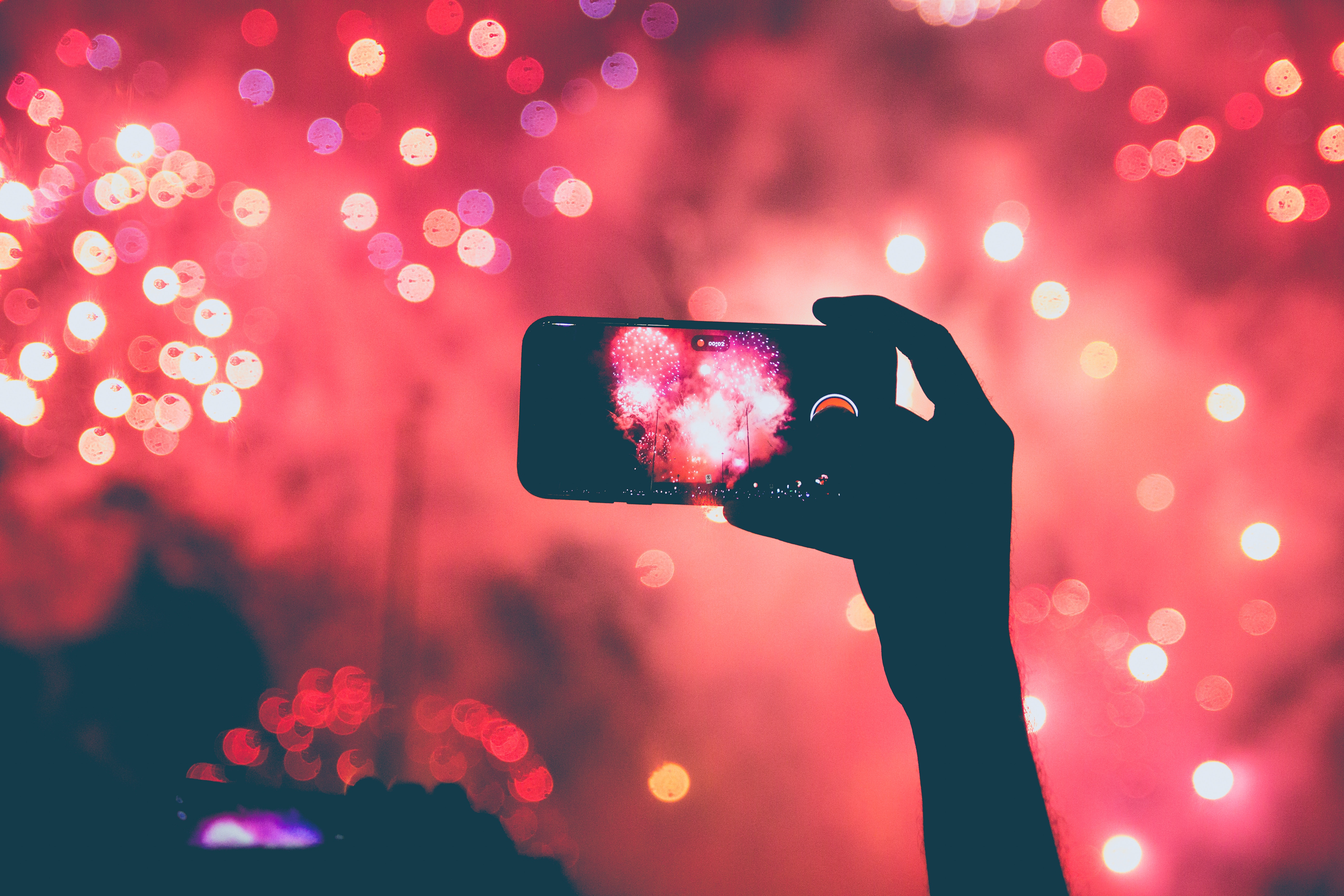 Hand holding iPhone recording fireworks at night HD Wallpaper