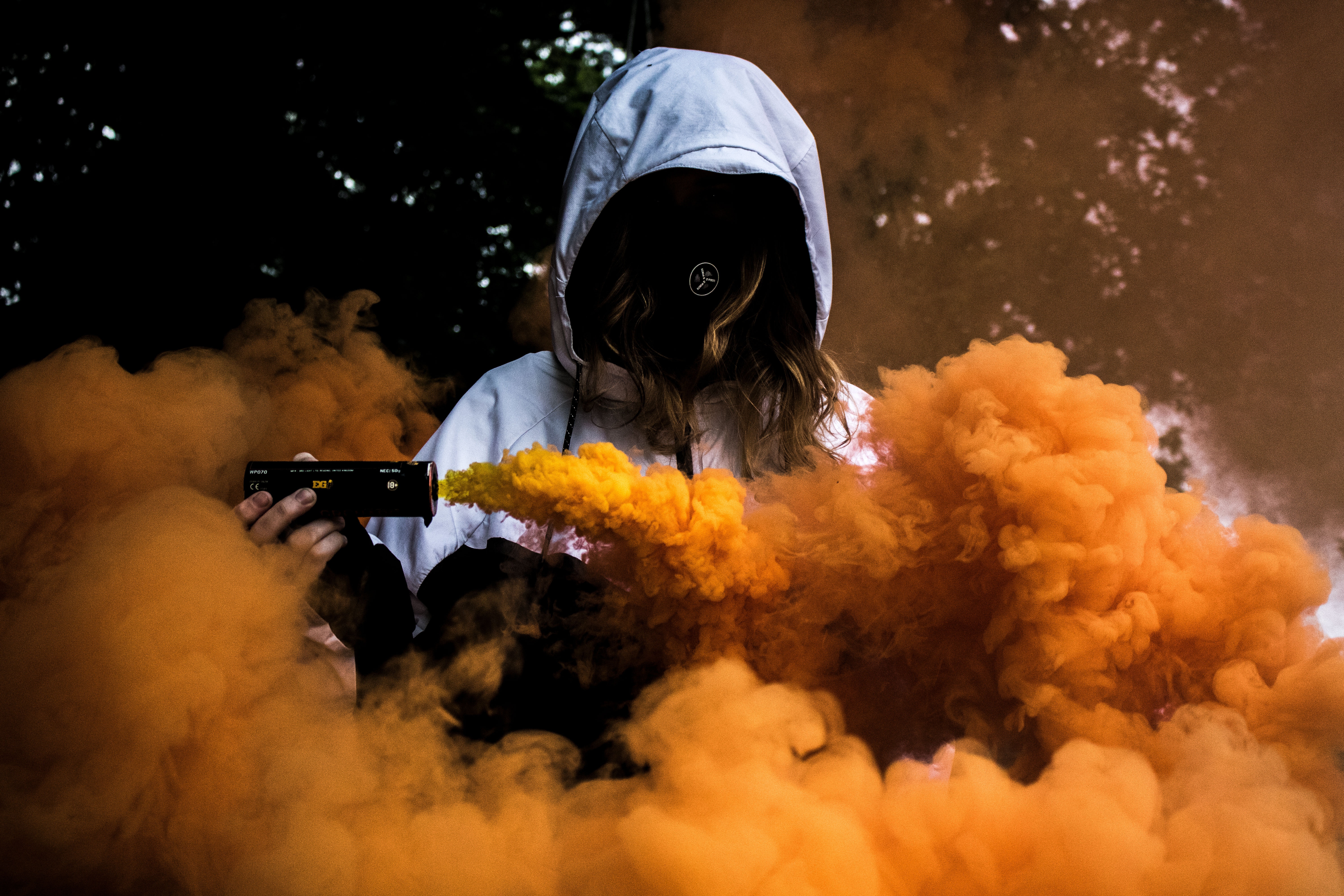 Person in hoodie holding smoke grenade with orange smoke HD Wallpaper