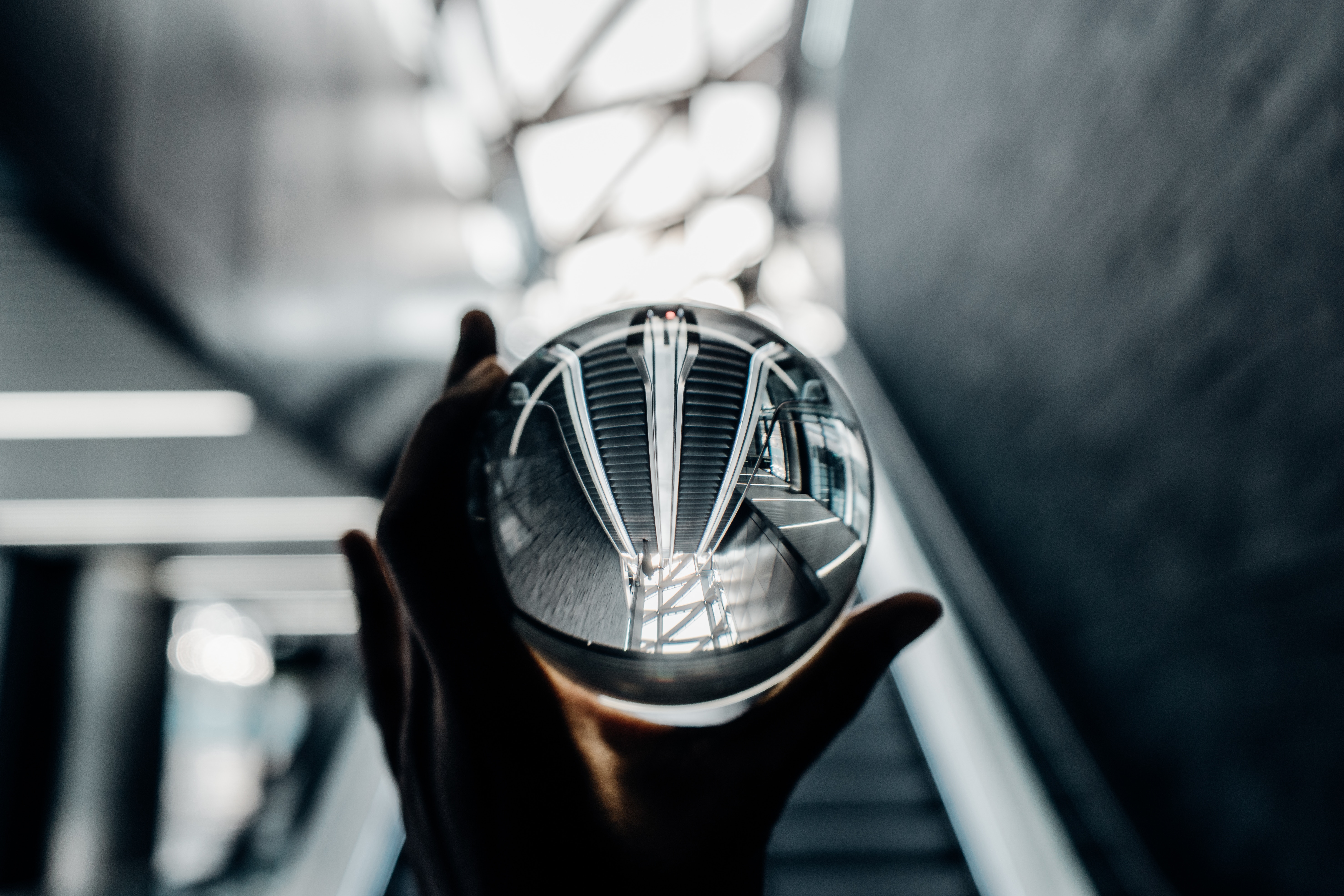 Hand holding glass ball reflecting escalator HD Wallpaper