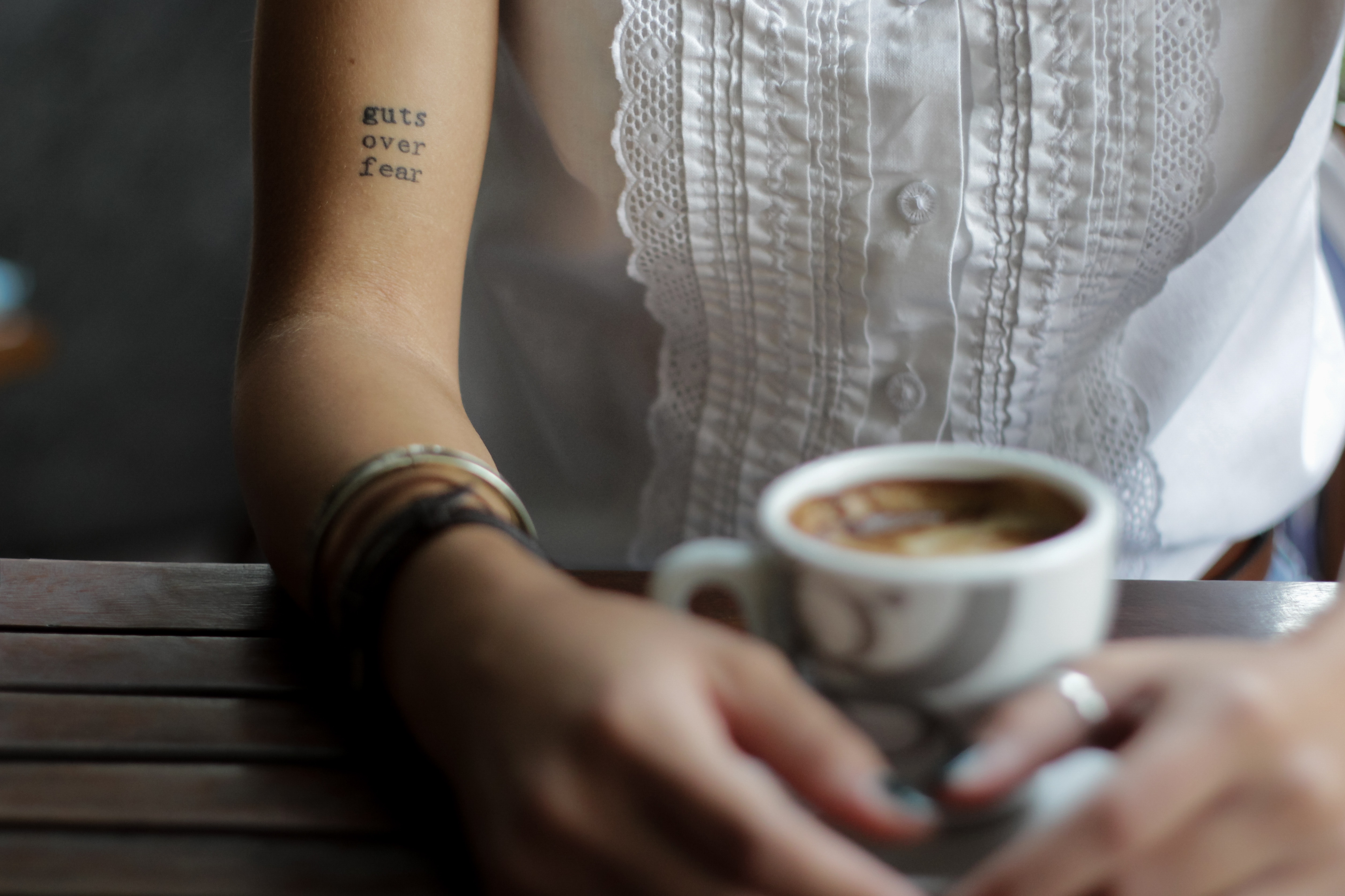 Woman with "guts over fear" tattoo holding coffee cup HD Wallpaper