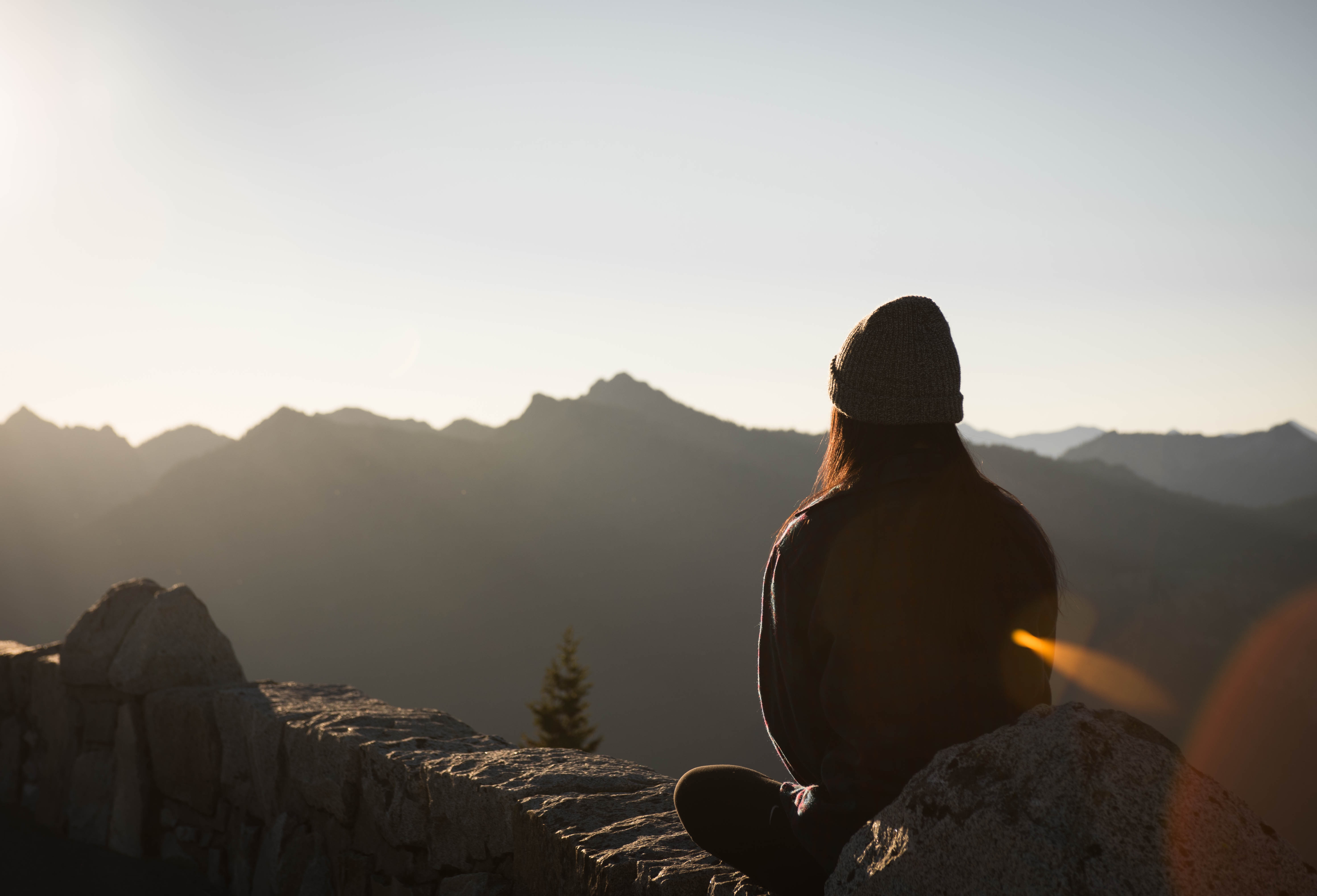 Woman meditating on a stone ledge overlooking mountains HD Wallpaper