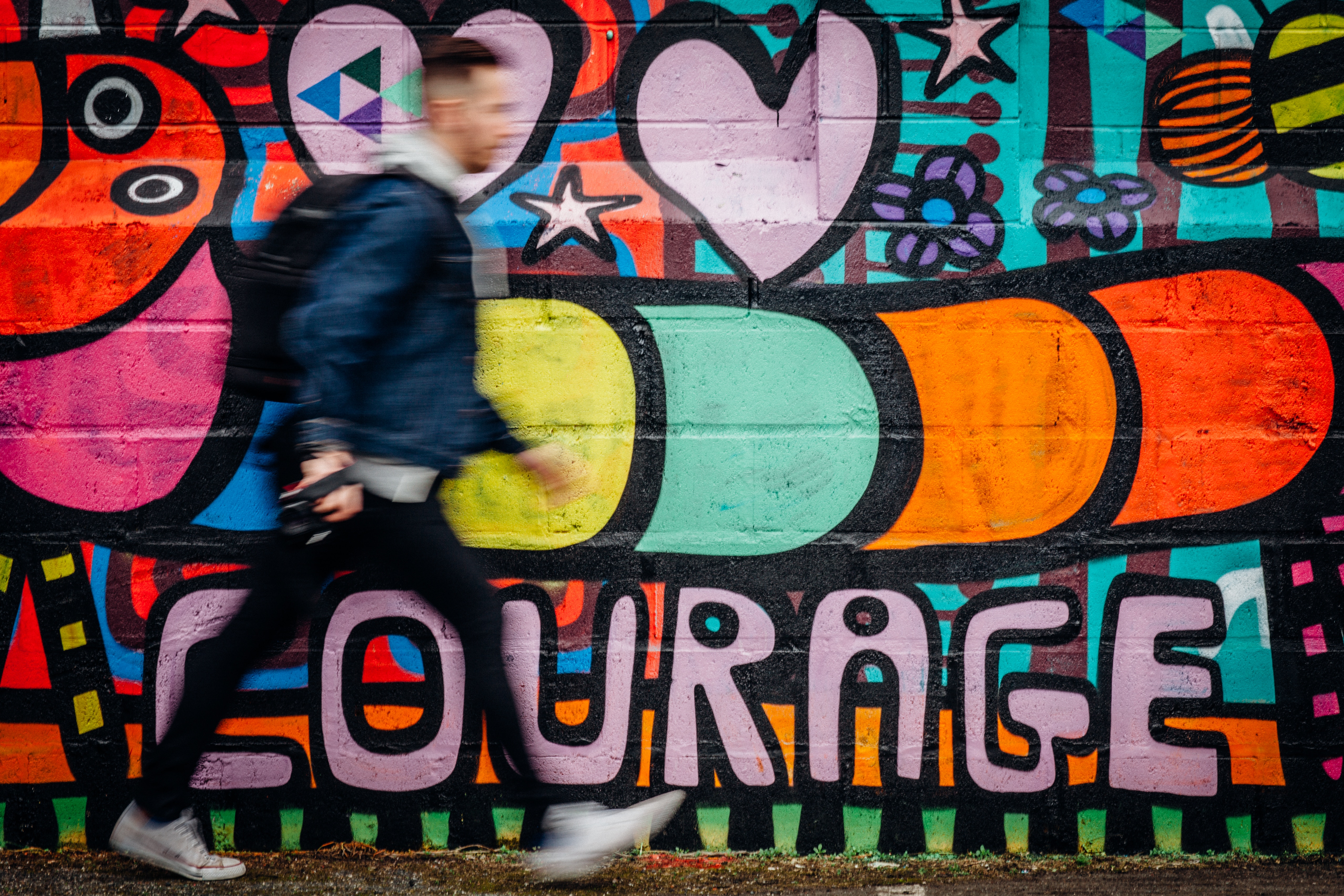 Man walking past colorful graffiti wall with the word courage HD Wallpaper