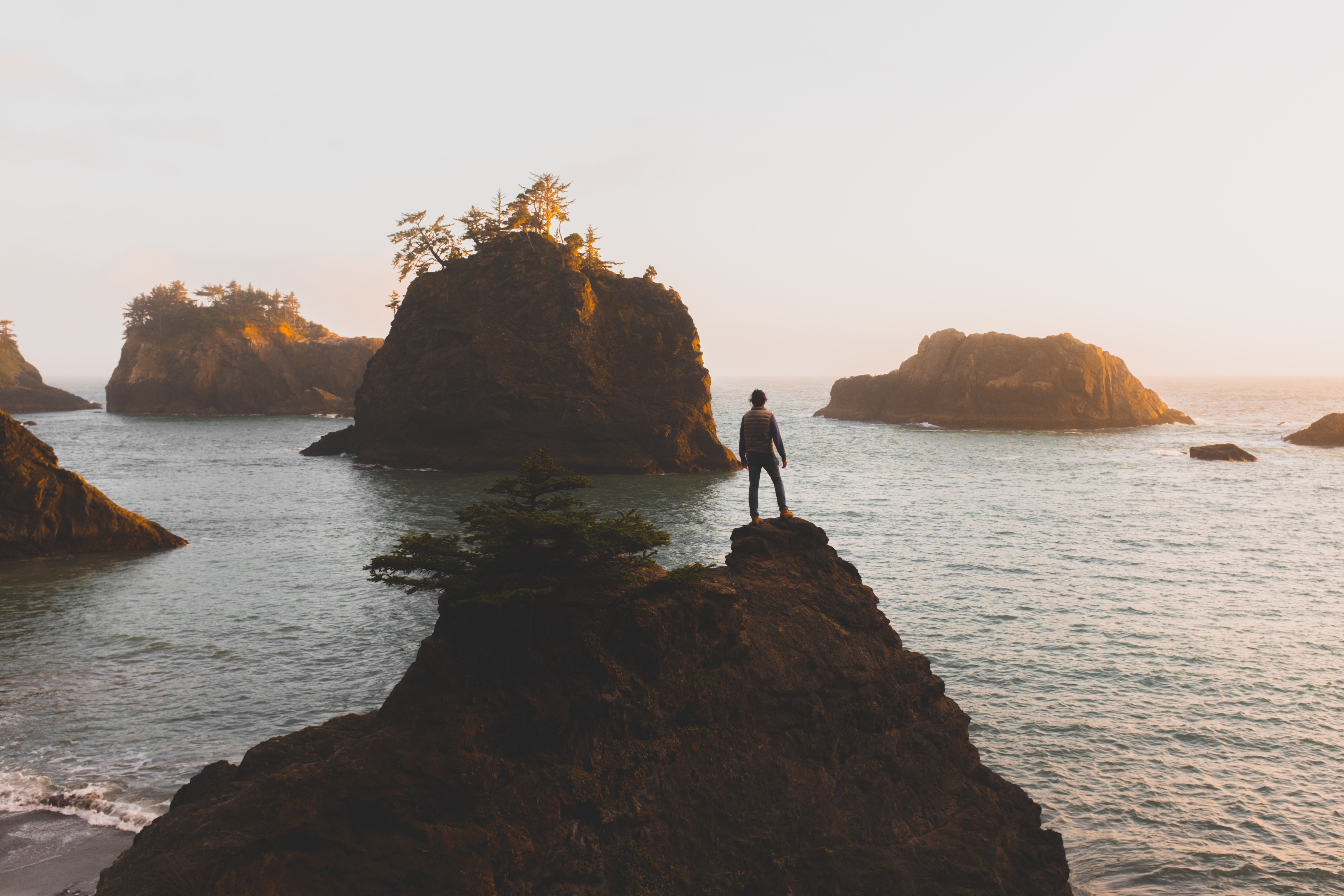 Man standing on a rock overlooking the ocean at sunset HD Wallpaper