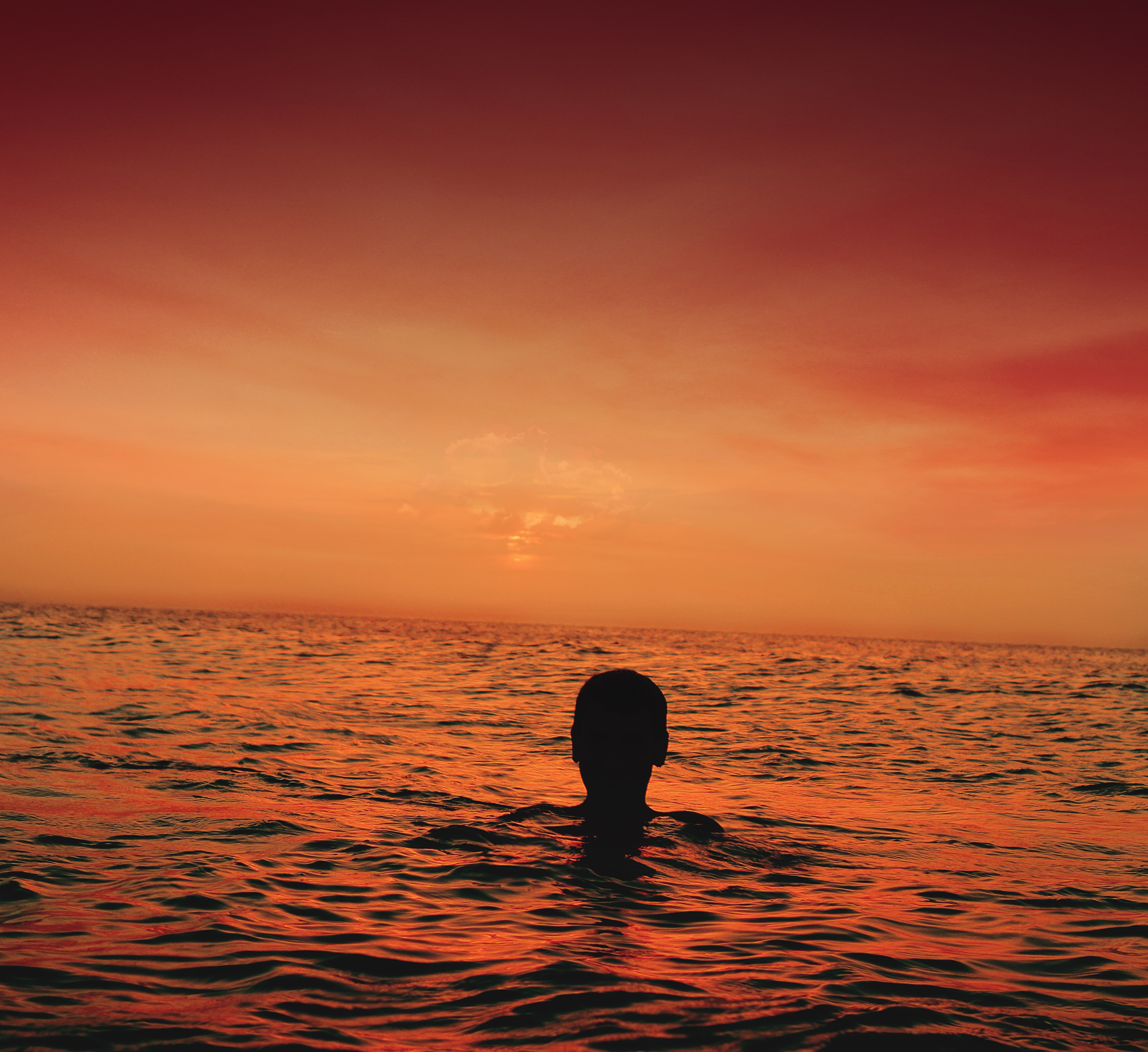 Silhouette of a person in the ocean at sunset HD Wallpaper